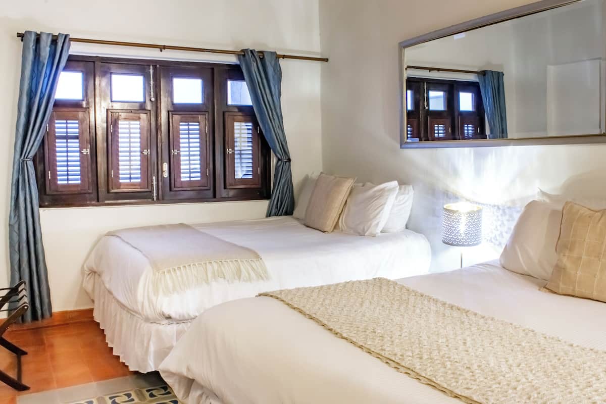 Ein Schlafzimmer mit zwei Betten, einem großen Spiegel und einem Fenster mit Fensterläden.