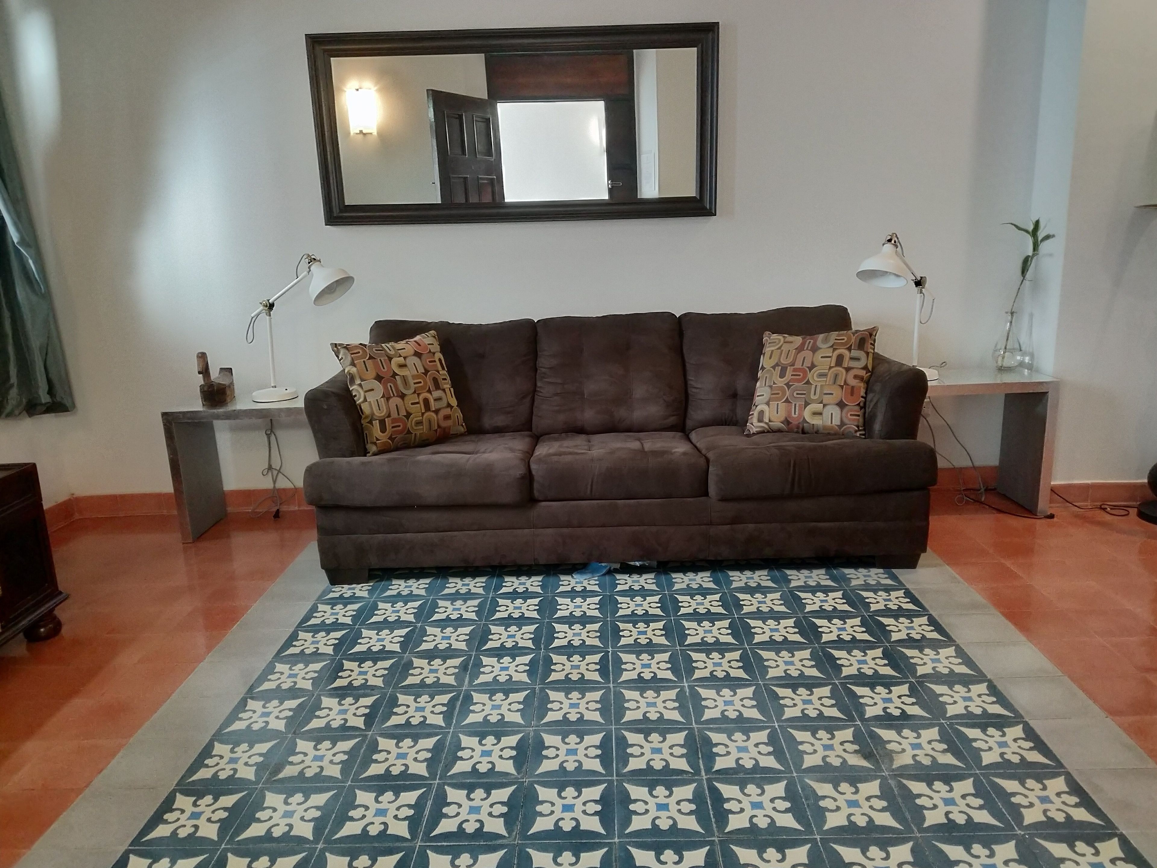 A living room with a brown sofa, patterned rug, two lamps, and a mirror on the wall.