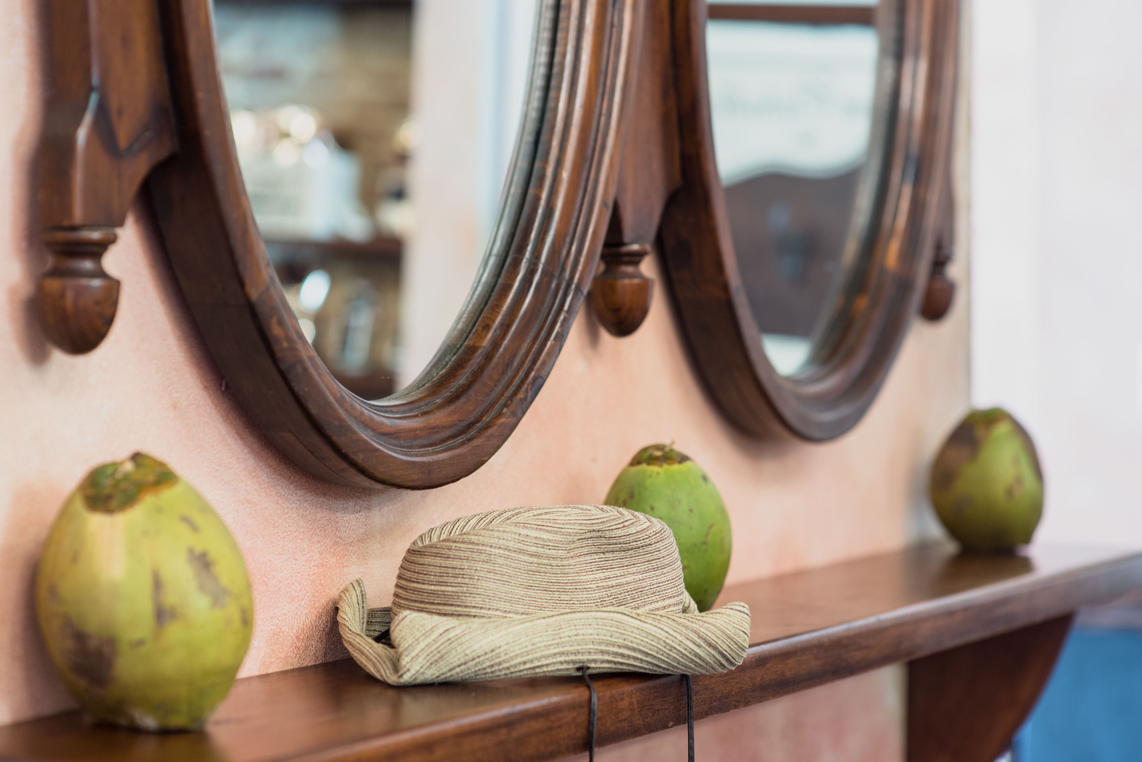 Une étagère en bois sur laquelle sont posés un chapeau tressé et deux fruits verts.