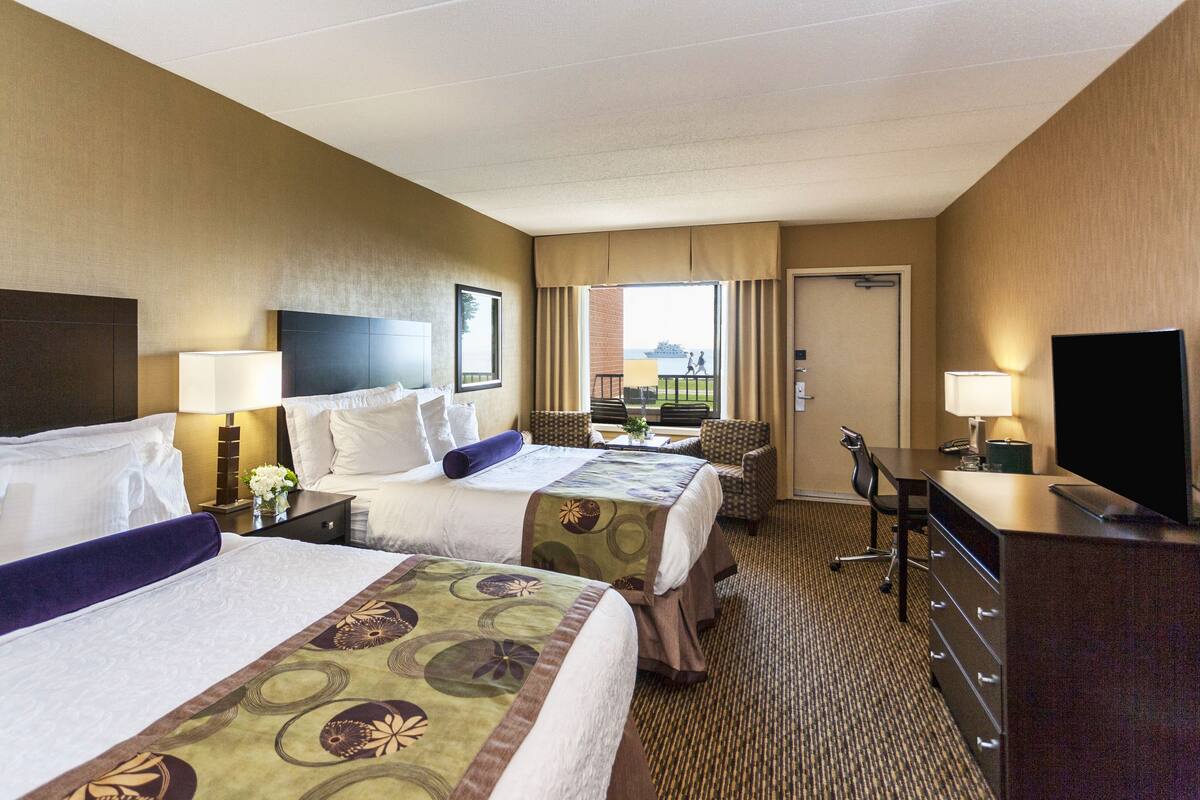 A hotel room with two beds, a desk, a TV, and a view of the outdoors.