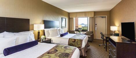 A hotel room with two beds, a desk, a TV, and a view of the outdoors.