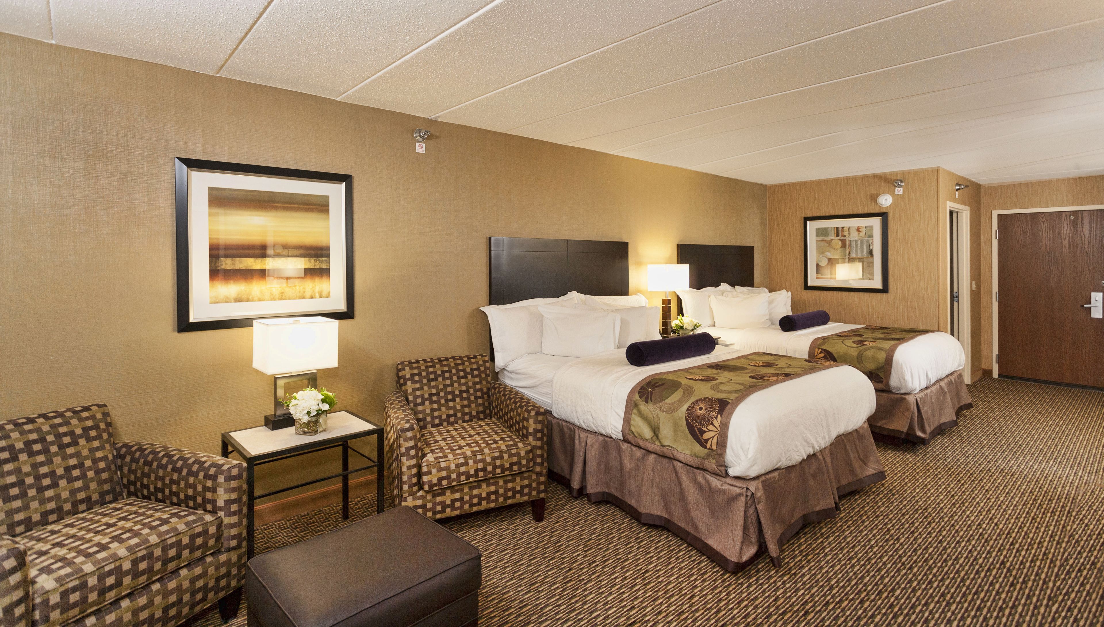 A hotel room with two beds, a sofa, a small table with a lamp, and a framed picture on the wall.
