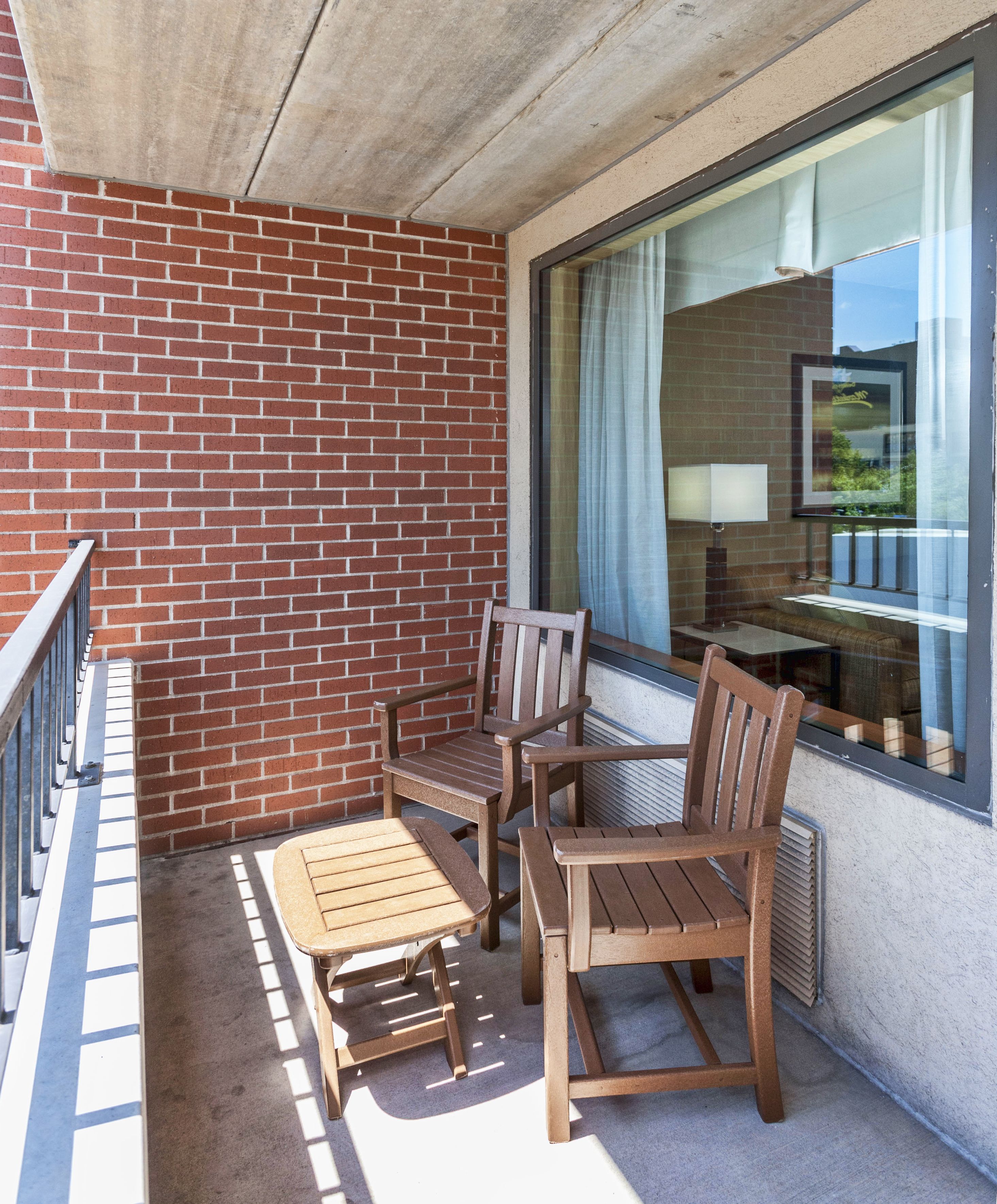 A balcony with a brick wall, a wooden table and chairs, and a window with a view of the outdoors.