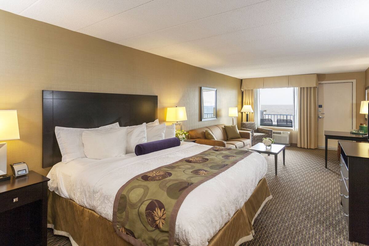 A hotel room with a large bed, two bedside tables, a desk, a chair, and a TV.