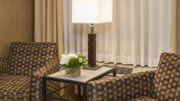 A hotel room with checkered armchairs, a table with a lamp, and a vase with flowers.
