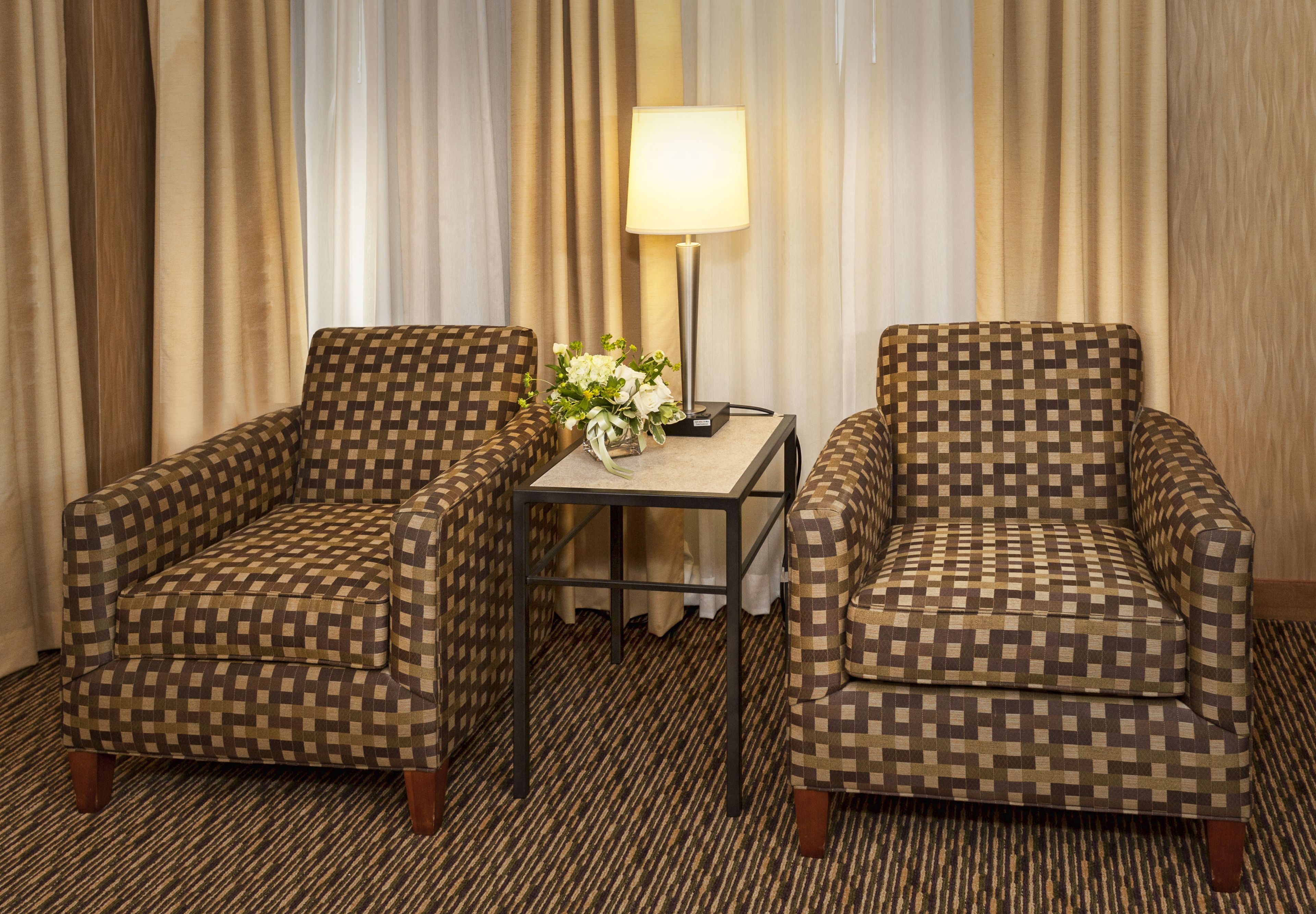 Two checkered armchairs, a small table with a lamp, and a vase with flowers.