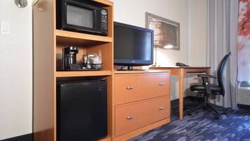 Een kleine hotelkamer met een kitchenette, inclusief een magnetron, koelkast en koffiezetapparaat. Er is een bureau met een computer en een stoel.