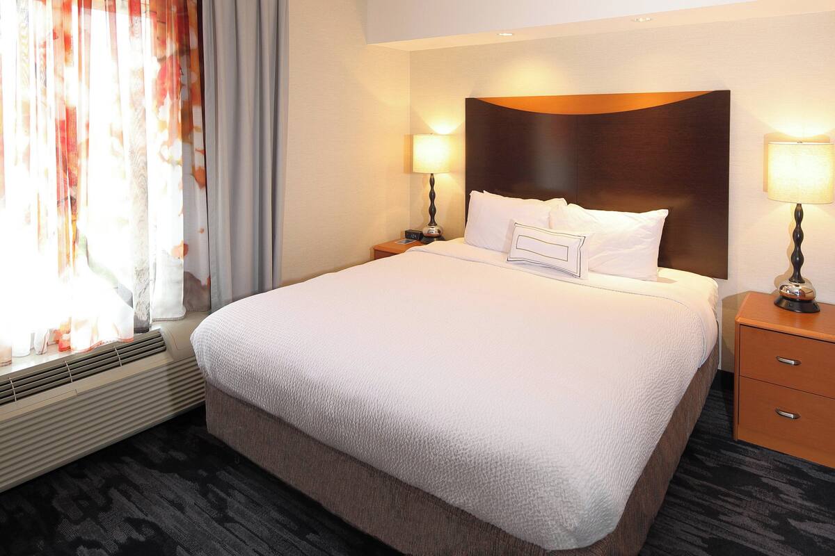Ein Hotelzimmer mit einem großen Bett, zwei Nachttischen mit Lampen, einem Fenster mit Vorhängen und einem fest installierten Heizkörper.