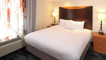 A hotel room with a large bed, two bedside tables with lamps, a window with curtains, and a wall-mounted heater.