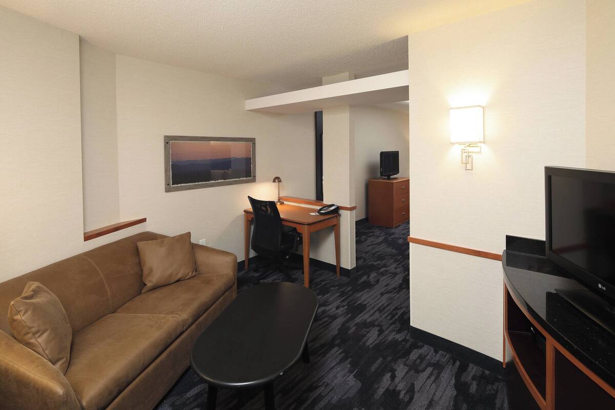 Ein Hotelzimmer mit braunem Ledersofa, einem kleinen Schreibtisch mit Stuhl, einem Flachbildfernseher und einem Bild an der Wand.