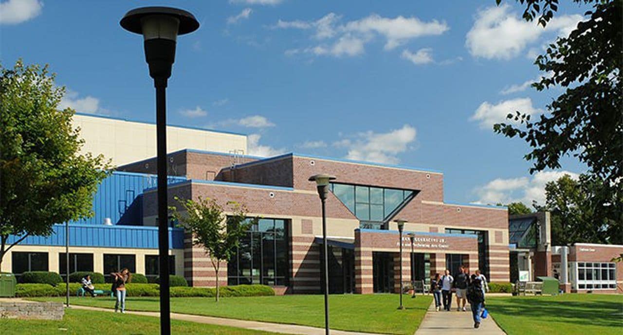 A modern building with a blue roof and brick facade, surrounded by a well-maintained lawn and a few people walking.