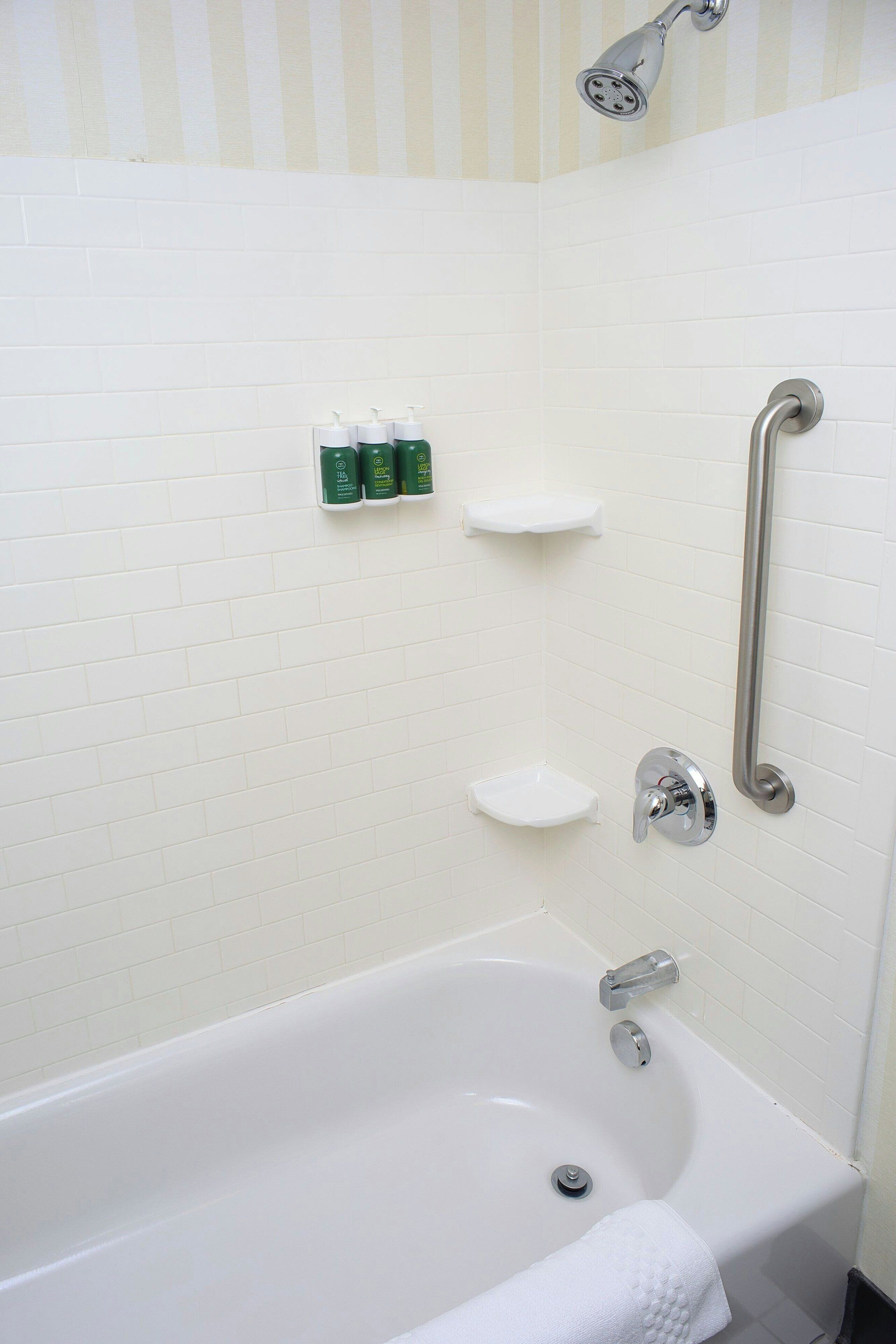 A white bathtub with a handheld showerhead, two white shelves, and a white towel.