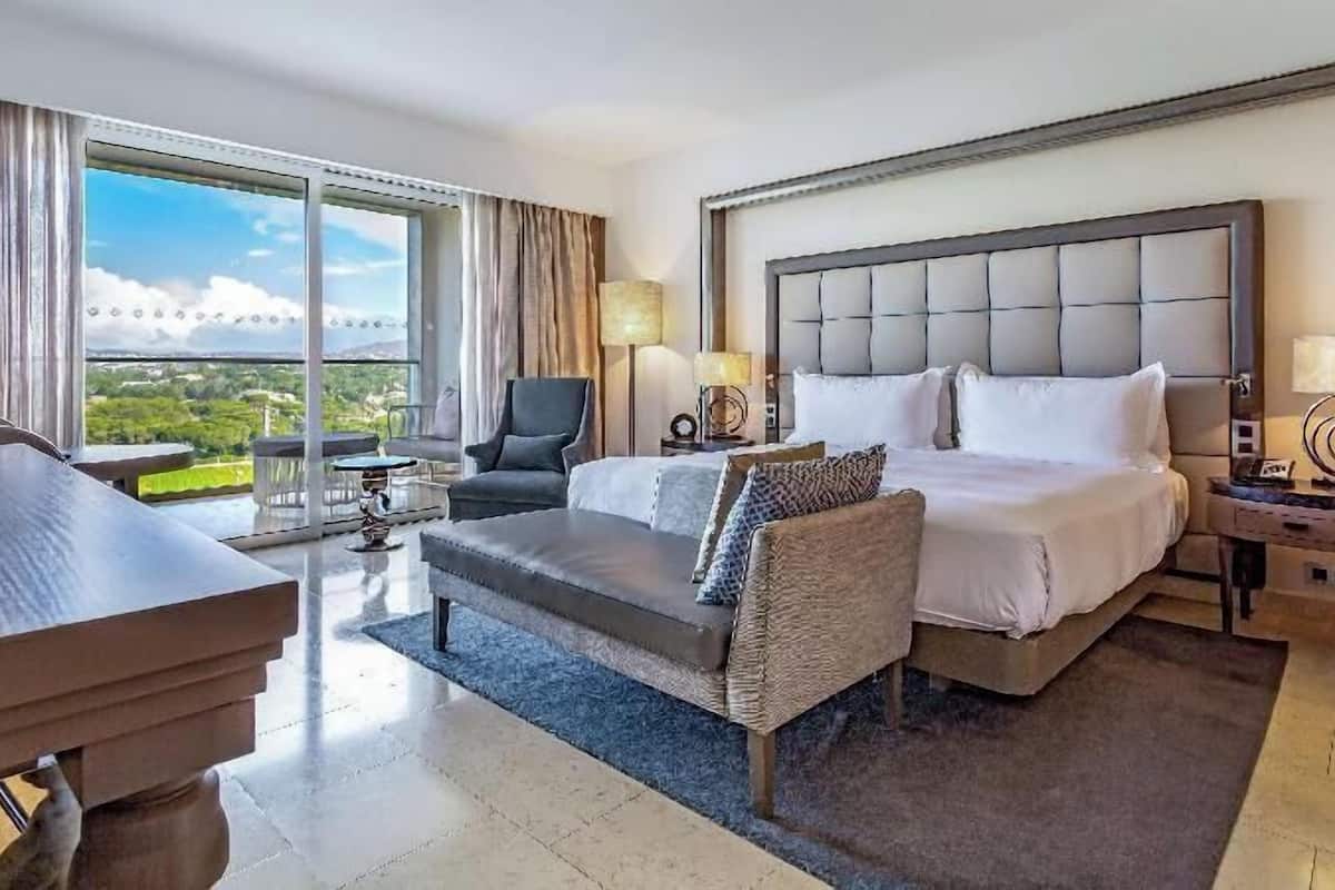 A hotel room with a bed, a desk, a chair, a sofa, and a view of the outdoors.