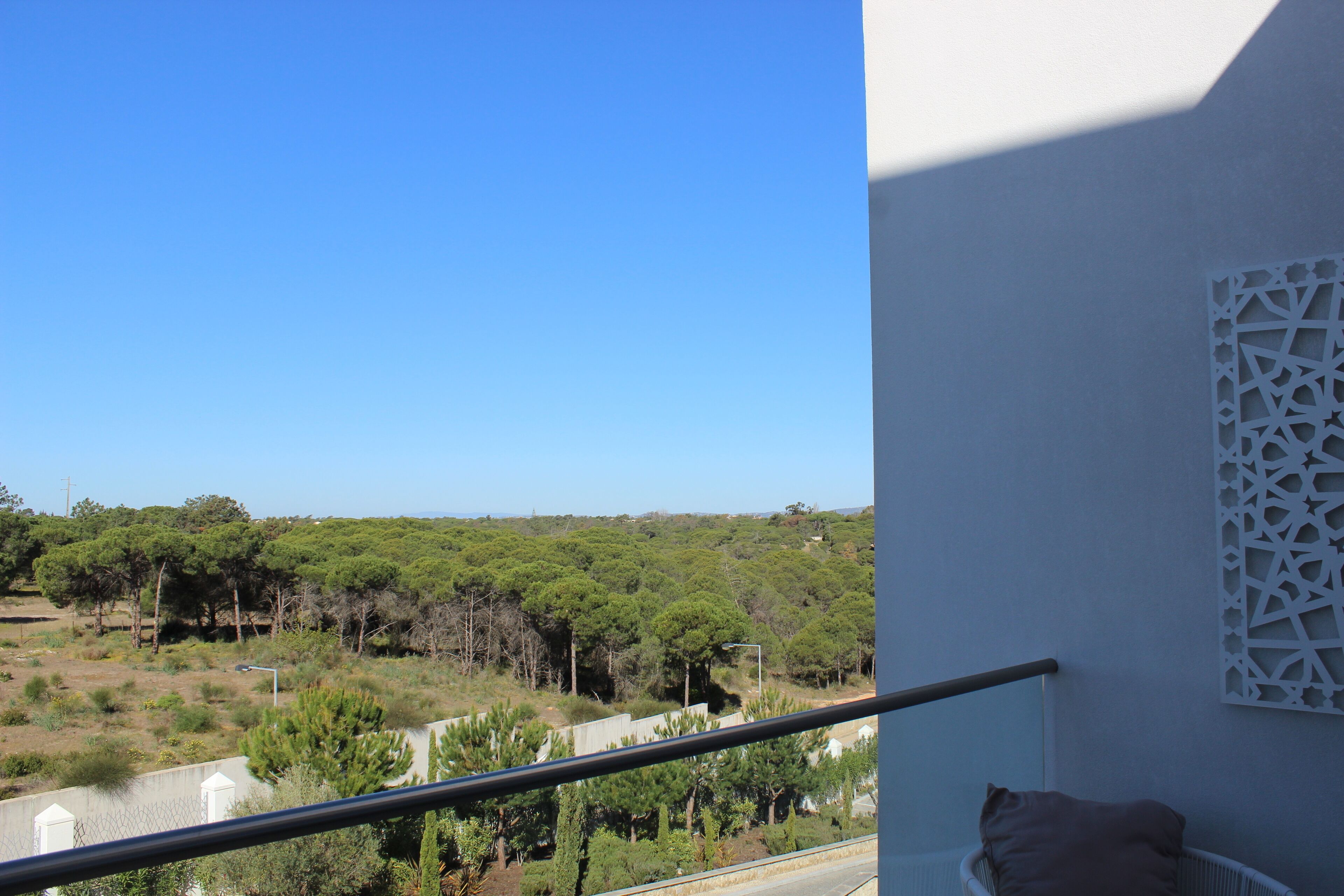 Un balcón con barandilla, vistas a un paisaje verde y una pared blanca con un diseño geométrico.
