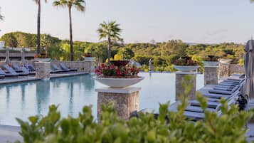 A pool area with lounge chairs, a flower planter, and a view of a lush landscape.