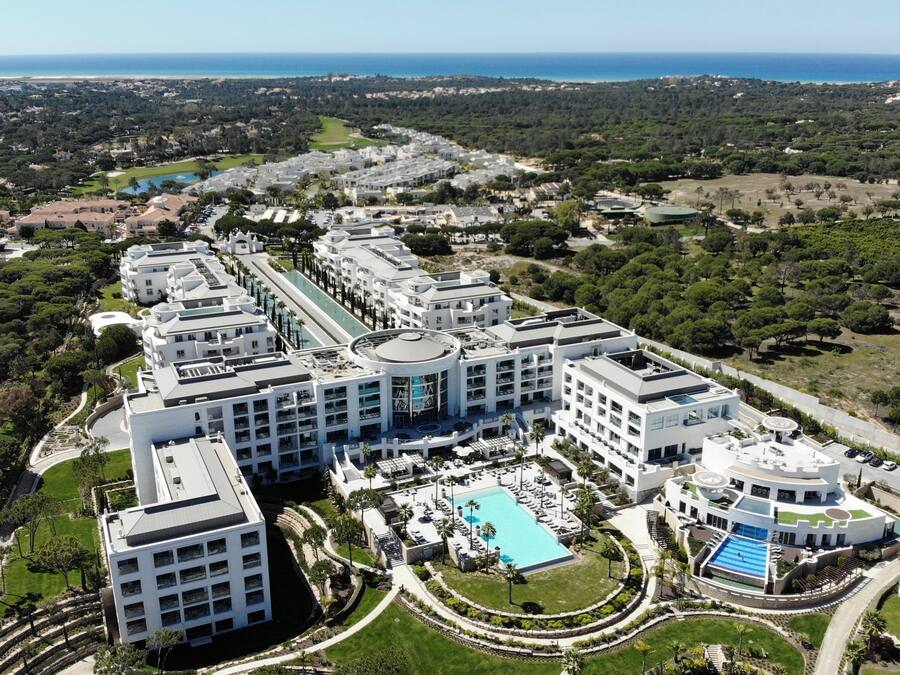 Un gran complejo hotelero moderno con varias edificaciones, una piscina central y vegetación circundante.