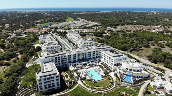 A large, modern hotel complex with multiple buildings, a central swimming pool, and surrounding greenery.
