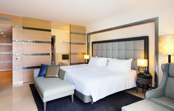 A modern hotel room with a large bed, a sofa, a chair, and a nightstand with a lamp. - Conrad Algarve (Loulé)