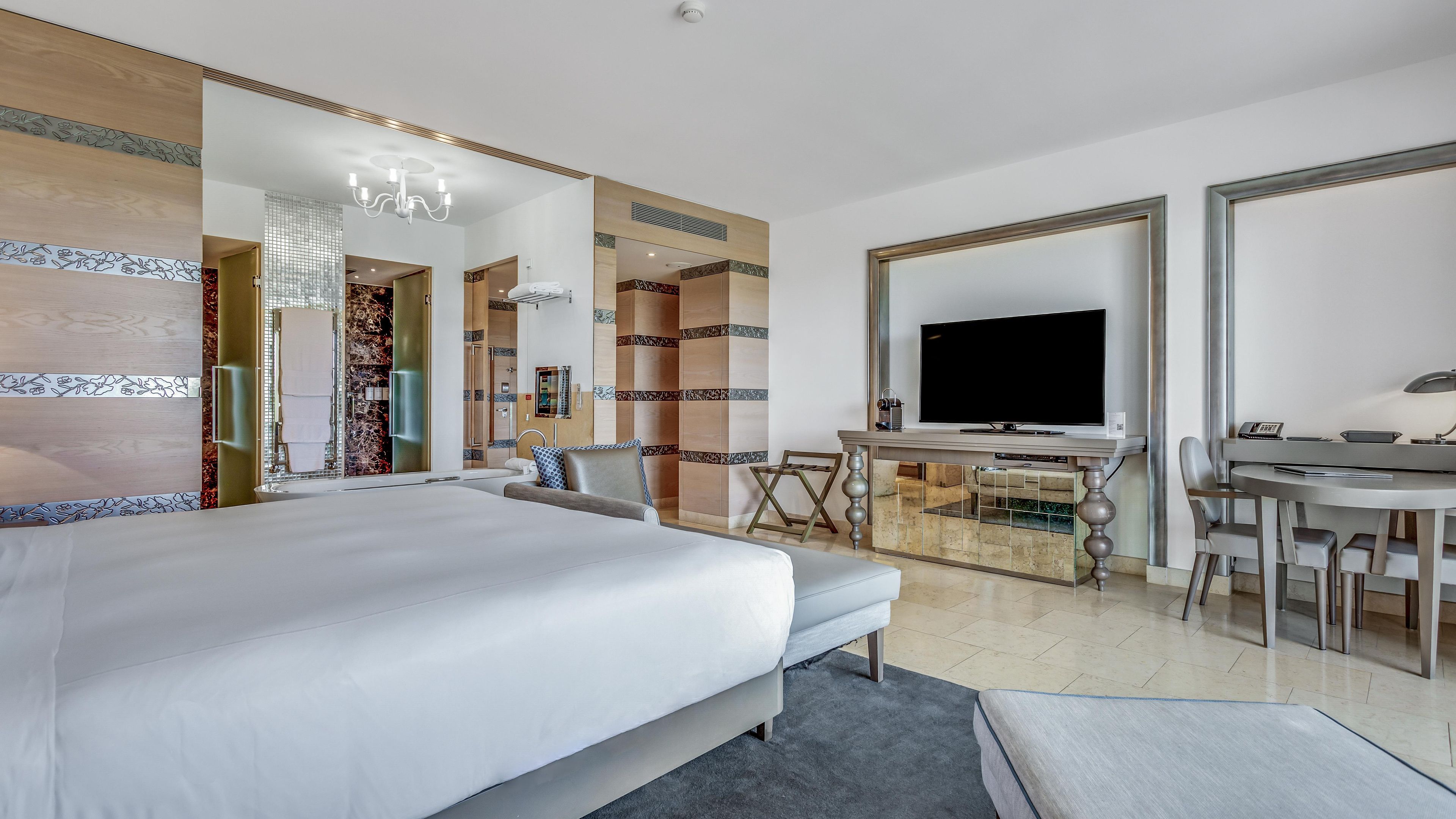 A modern hotel room with a large bed, a desk, a television, and a bathroom with a shower and toilet.