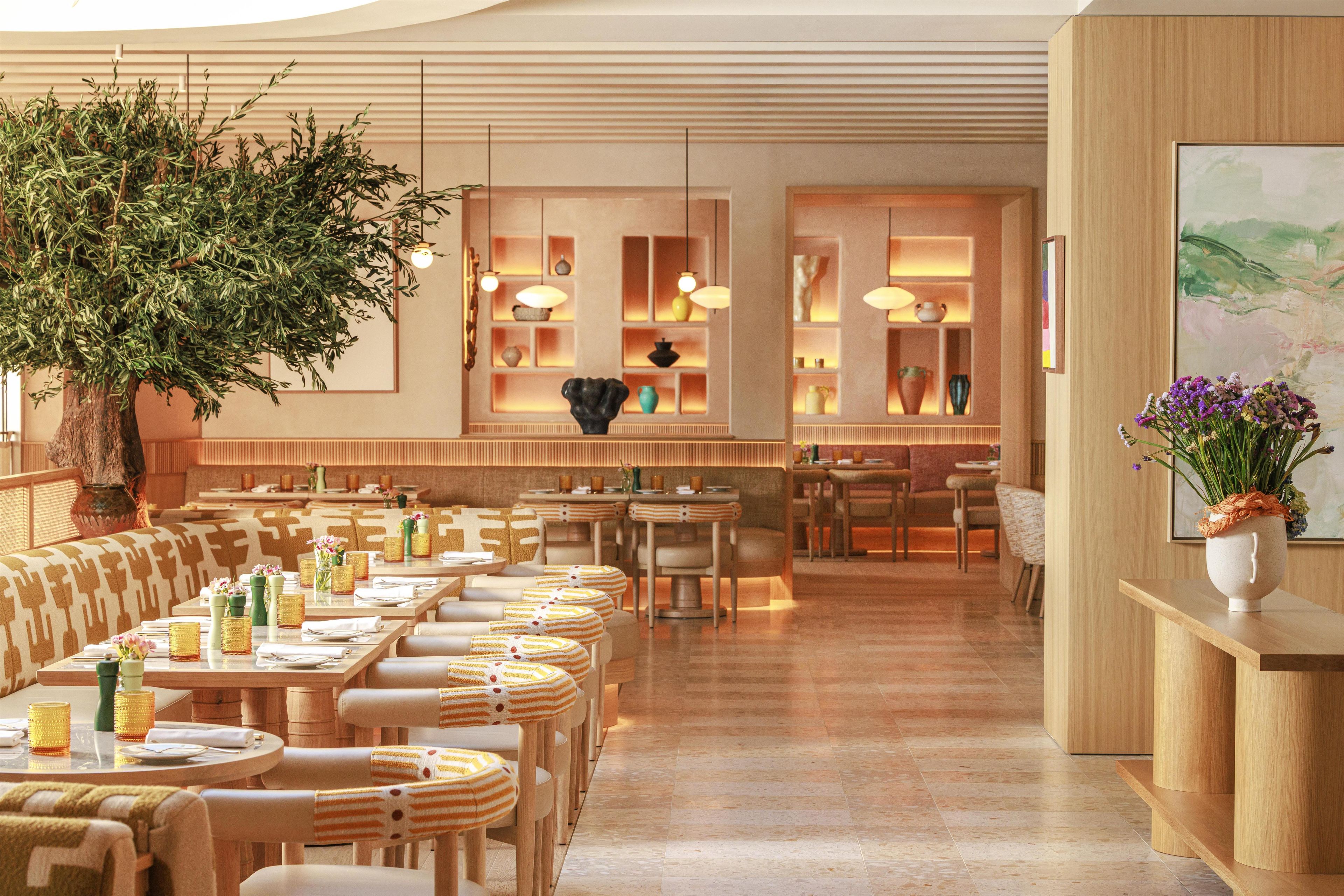 A restaurant with wooden furniture, a large tree, and shelves with decorative items.