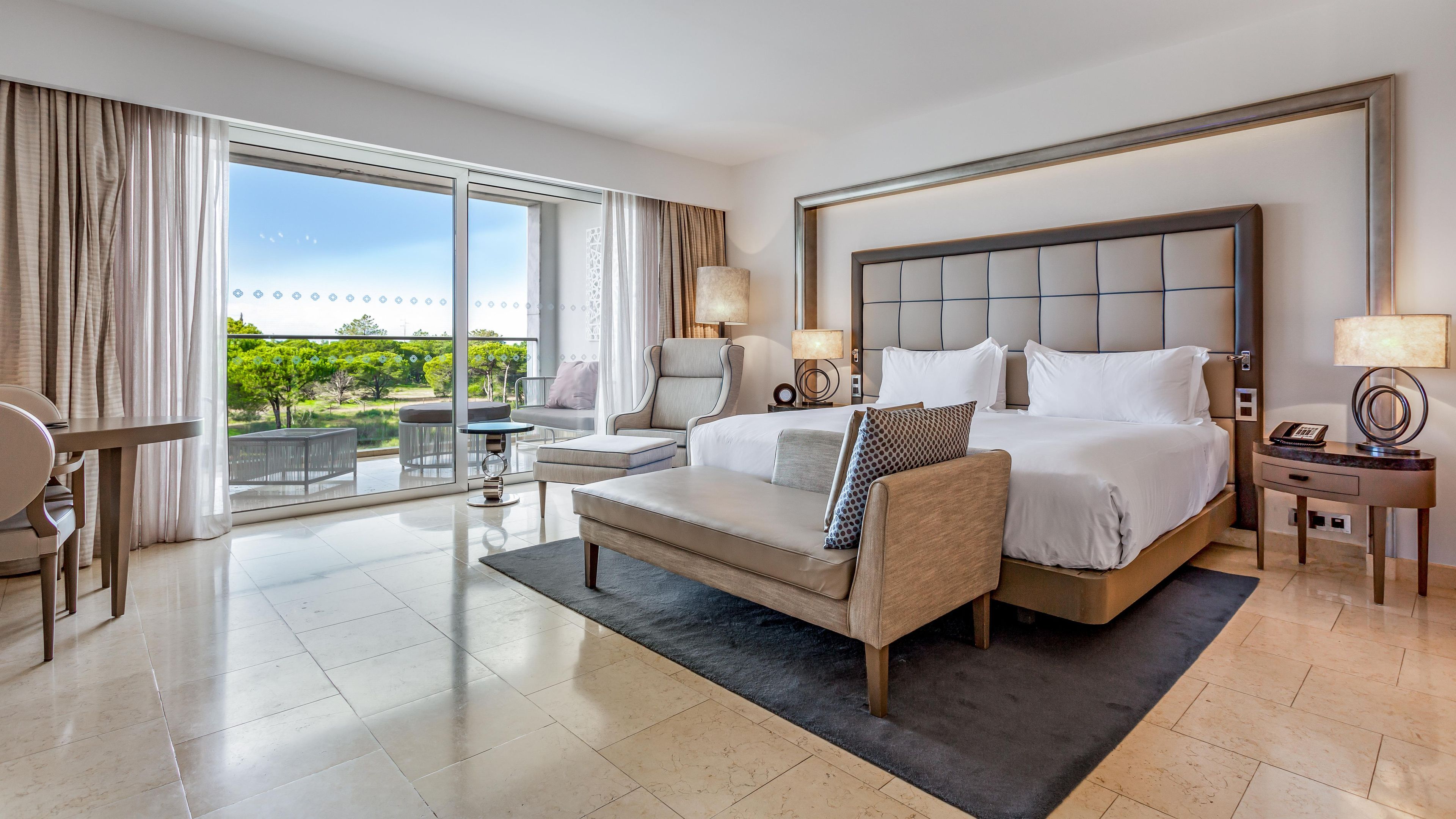 Habitación de hotel con una cama grande, un sofá, un escritorio y un balcón con vistas a zonas verdes.