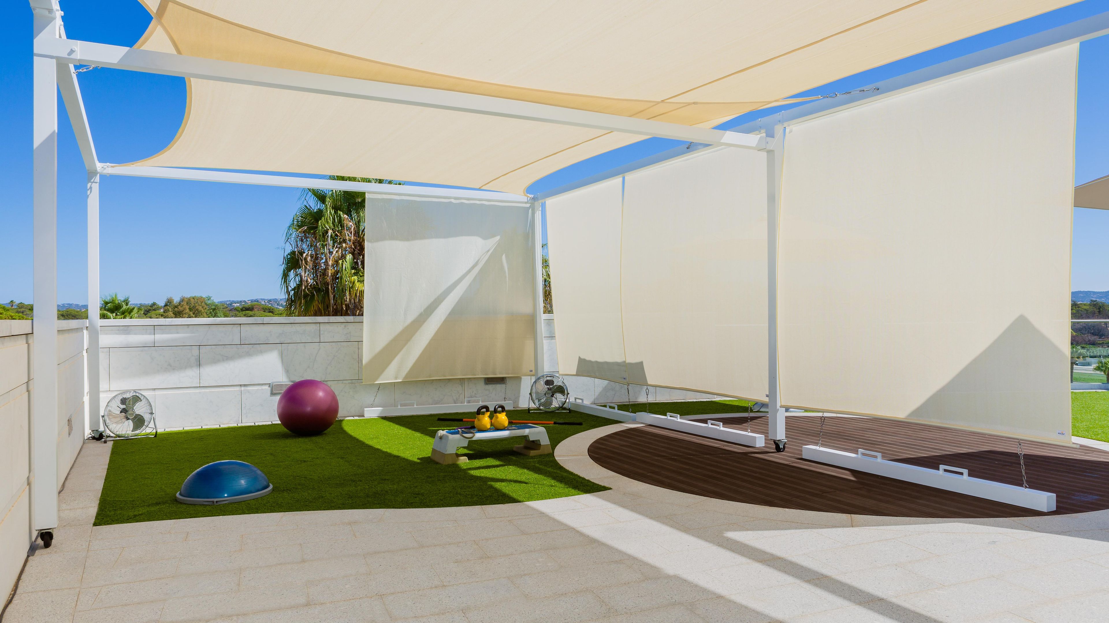 An outdoor area with artificial grass, exercise equipment, and a shaded structure.