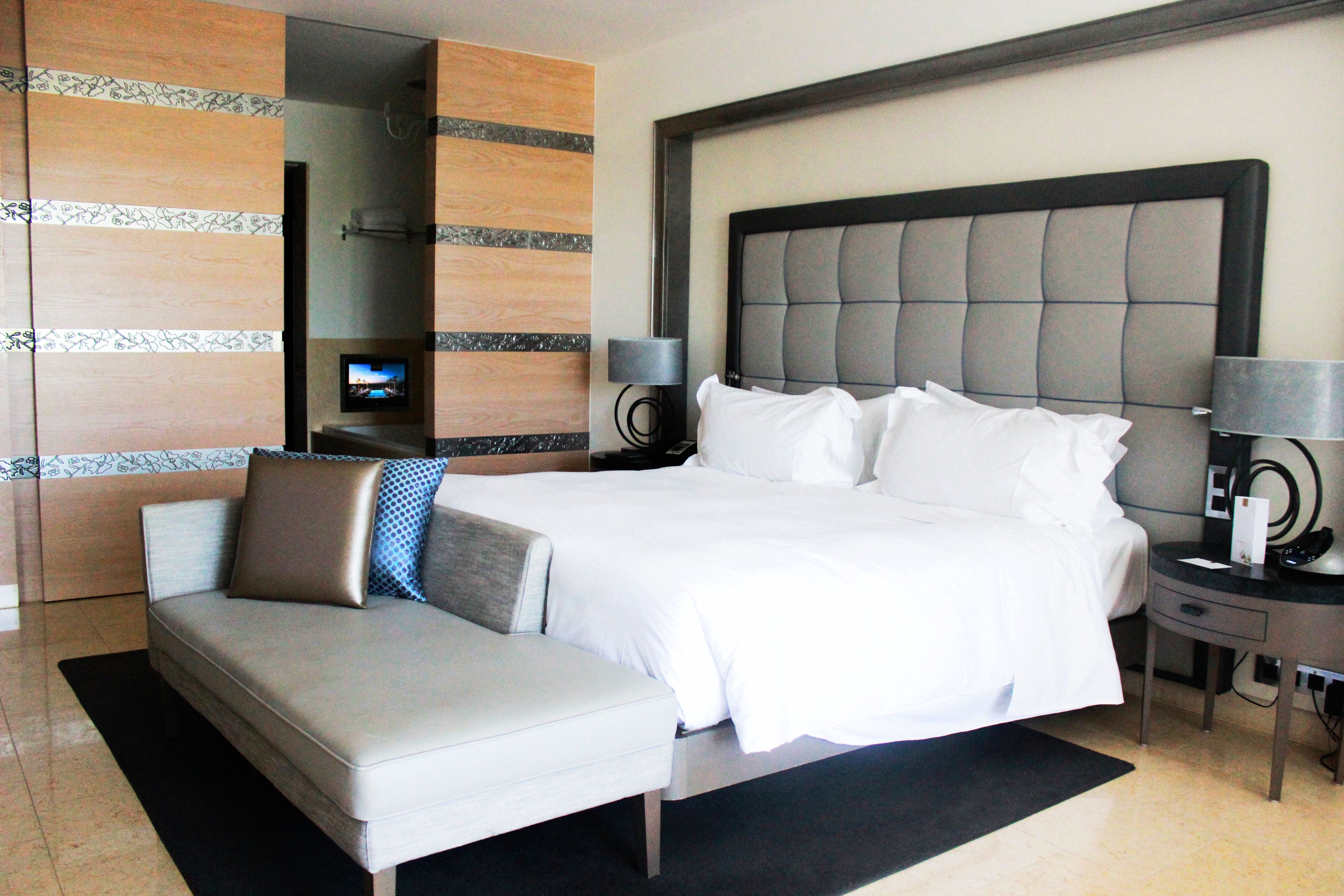 A hotel room with a large bed, a sofa, a TV, and a desk with a lamp.