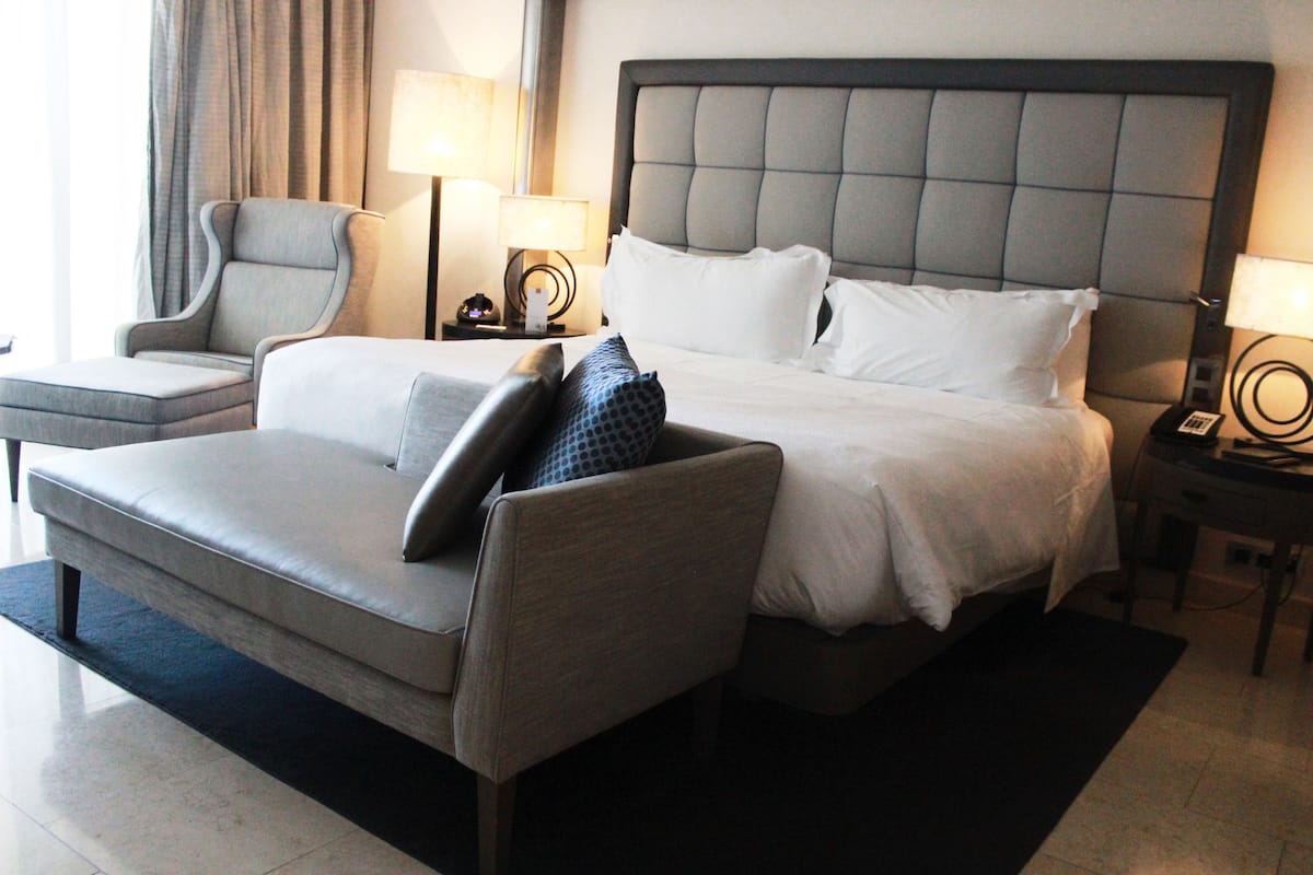 A hotel room with a large bed, a sofa, a chair, and two bedside tables with lamps.