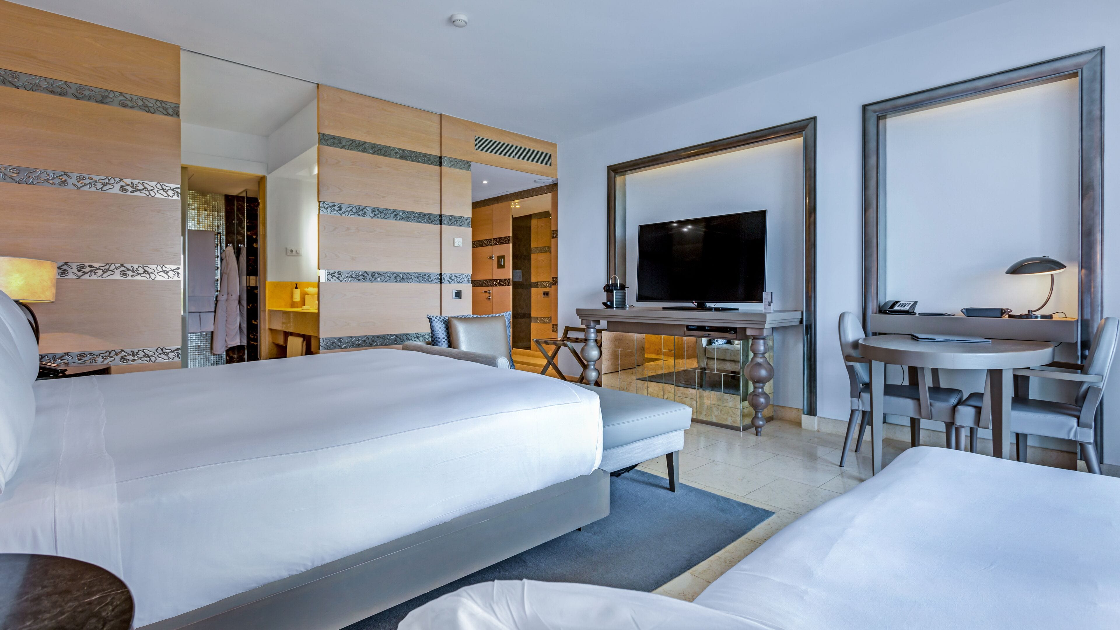 A hotel room with a large bed, a desk with a TV, and a seating area with chairs.