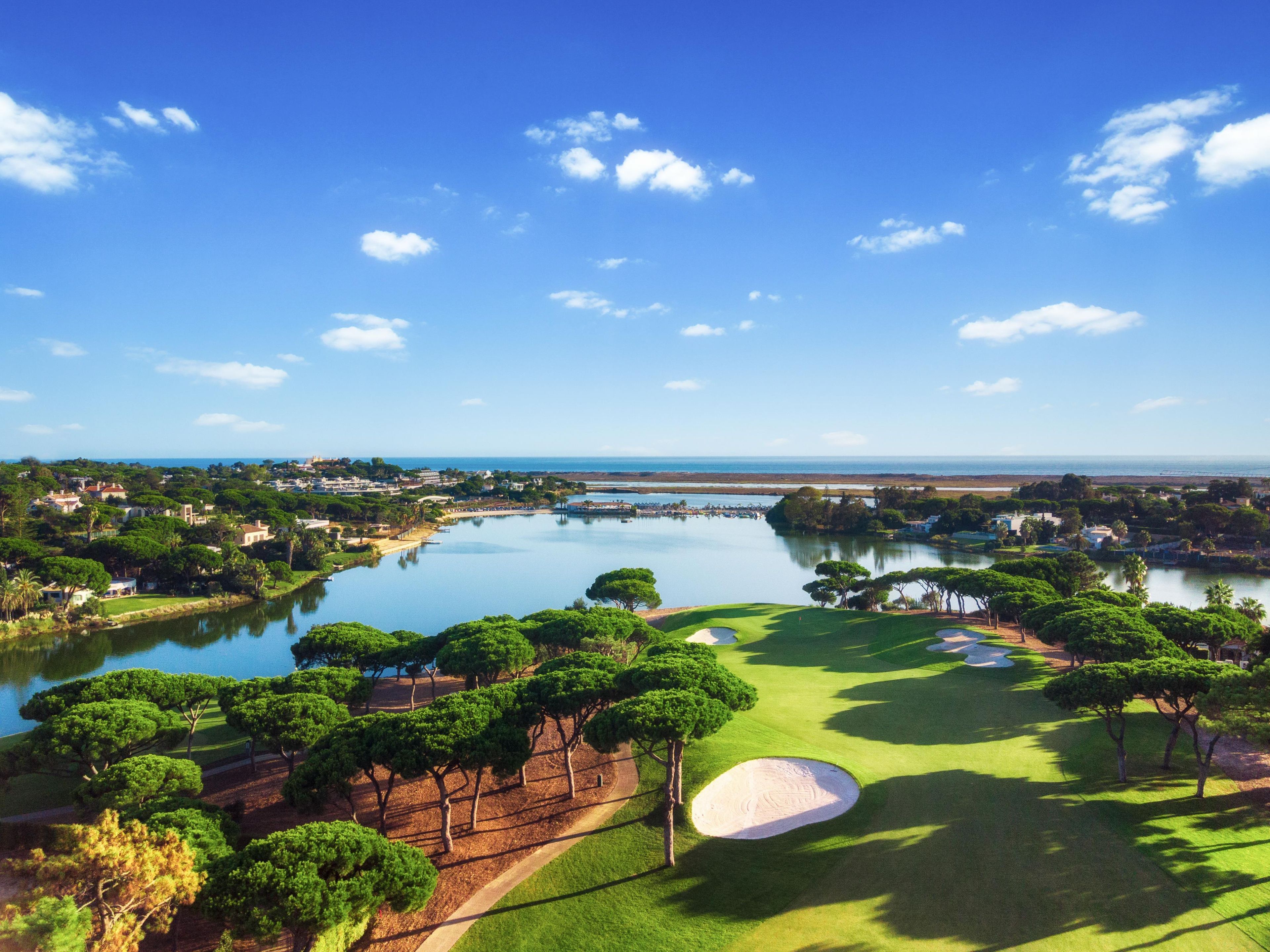 A golf course with a large pond, trees, and a clear sky.