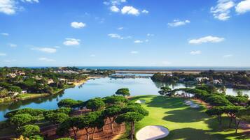 A golf course with a large pond, trees, and a clear sky.