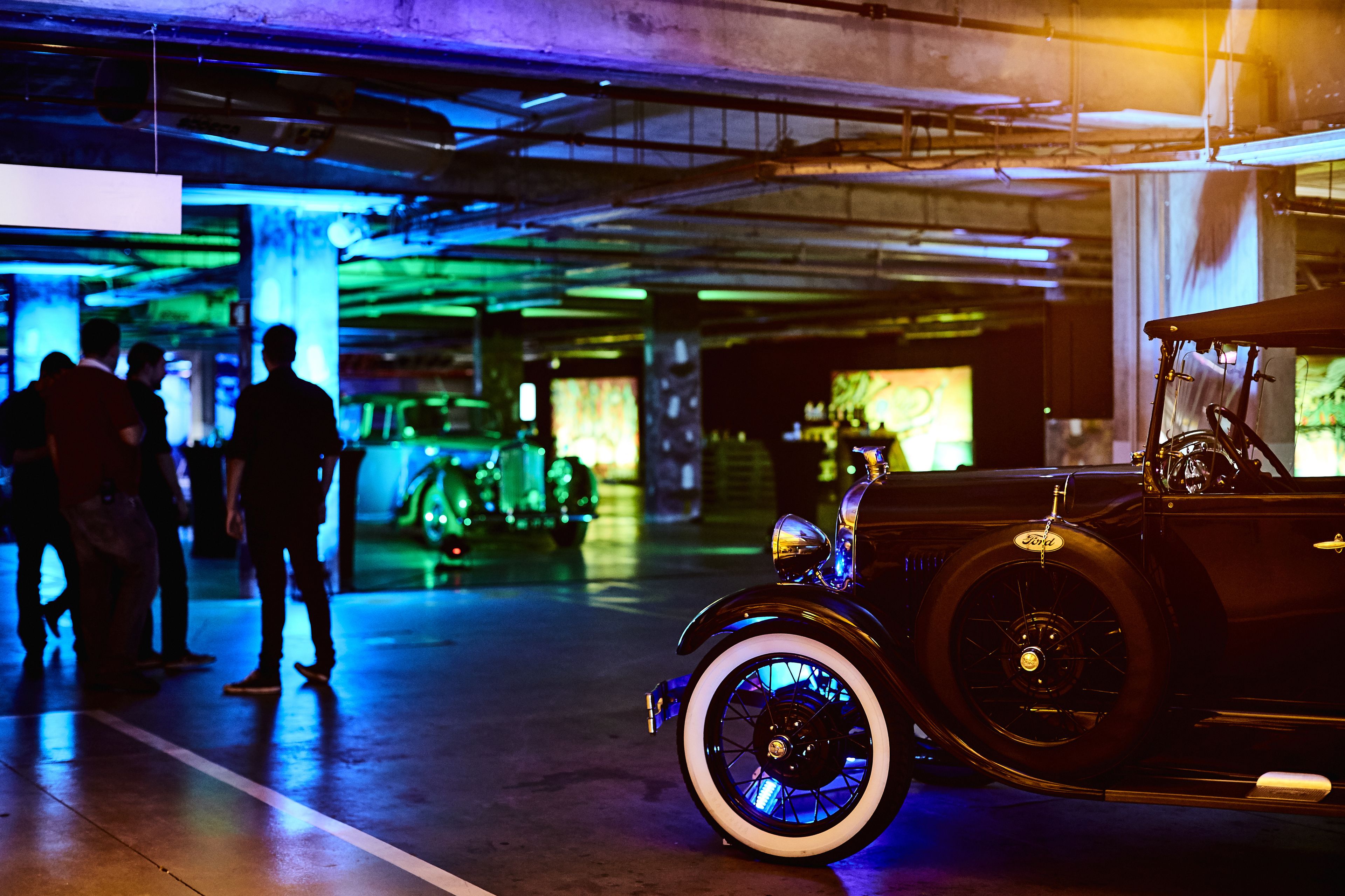 Un coche antiguo en un estacionamiento poco iluminado, con gente alrededor.
