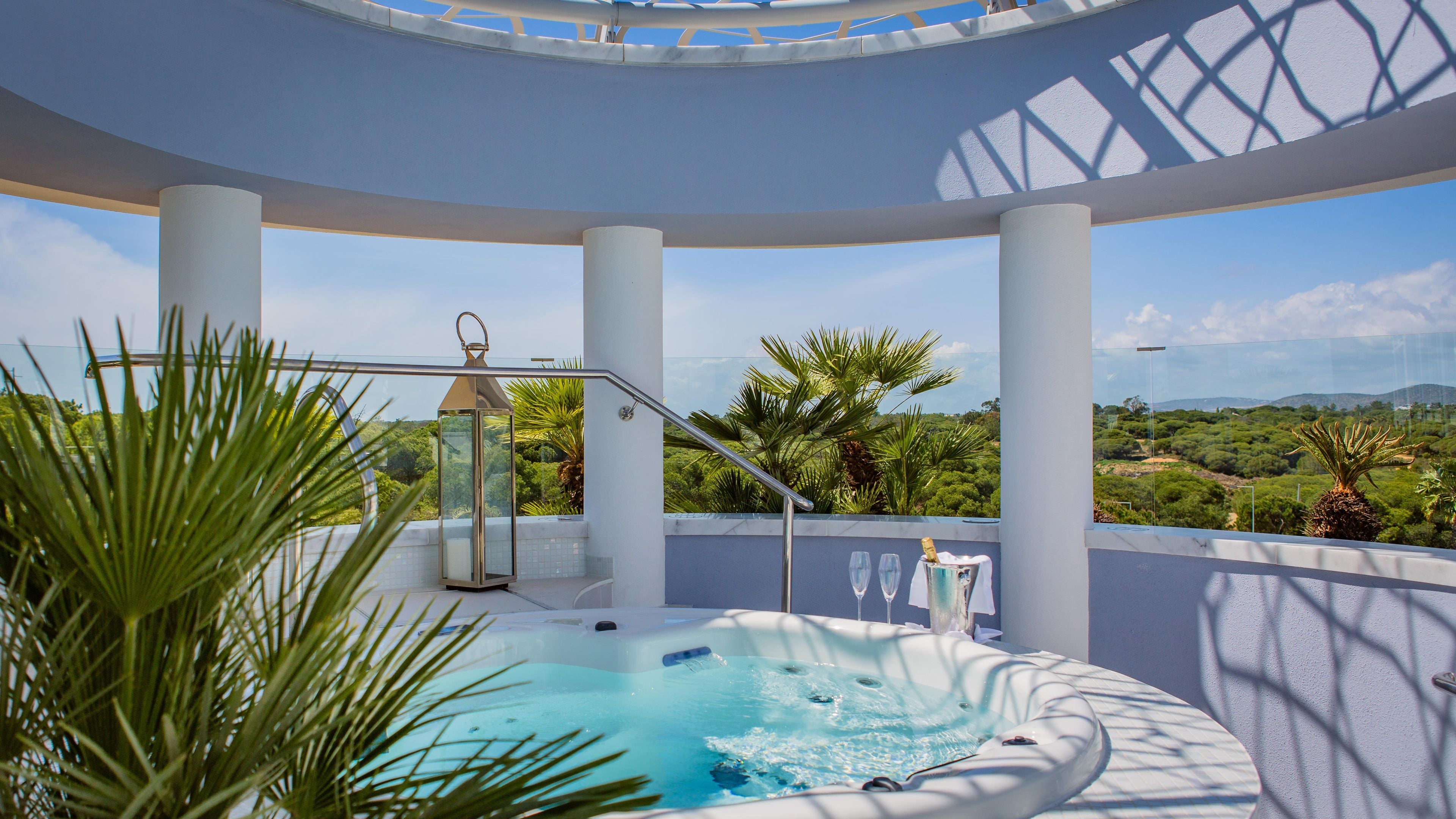 Un jacuzzi con vistas despejadas del paisaje, rodeado de columnas blancas y una barandilla de vidrio.