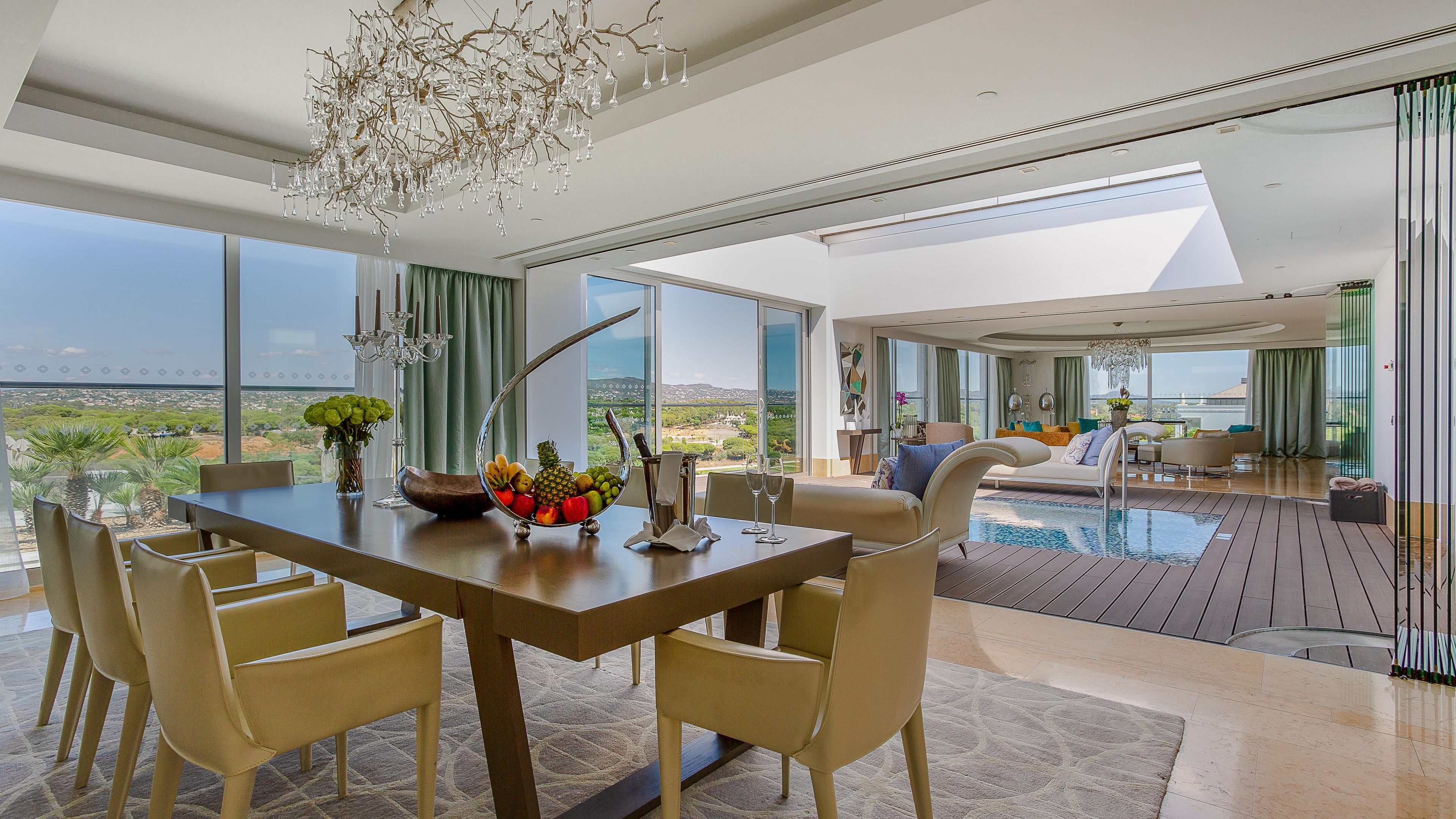 A modern dining area with a view of the landscape, a pool, and a living area with a sofa and table.