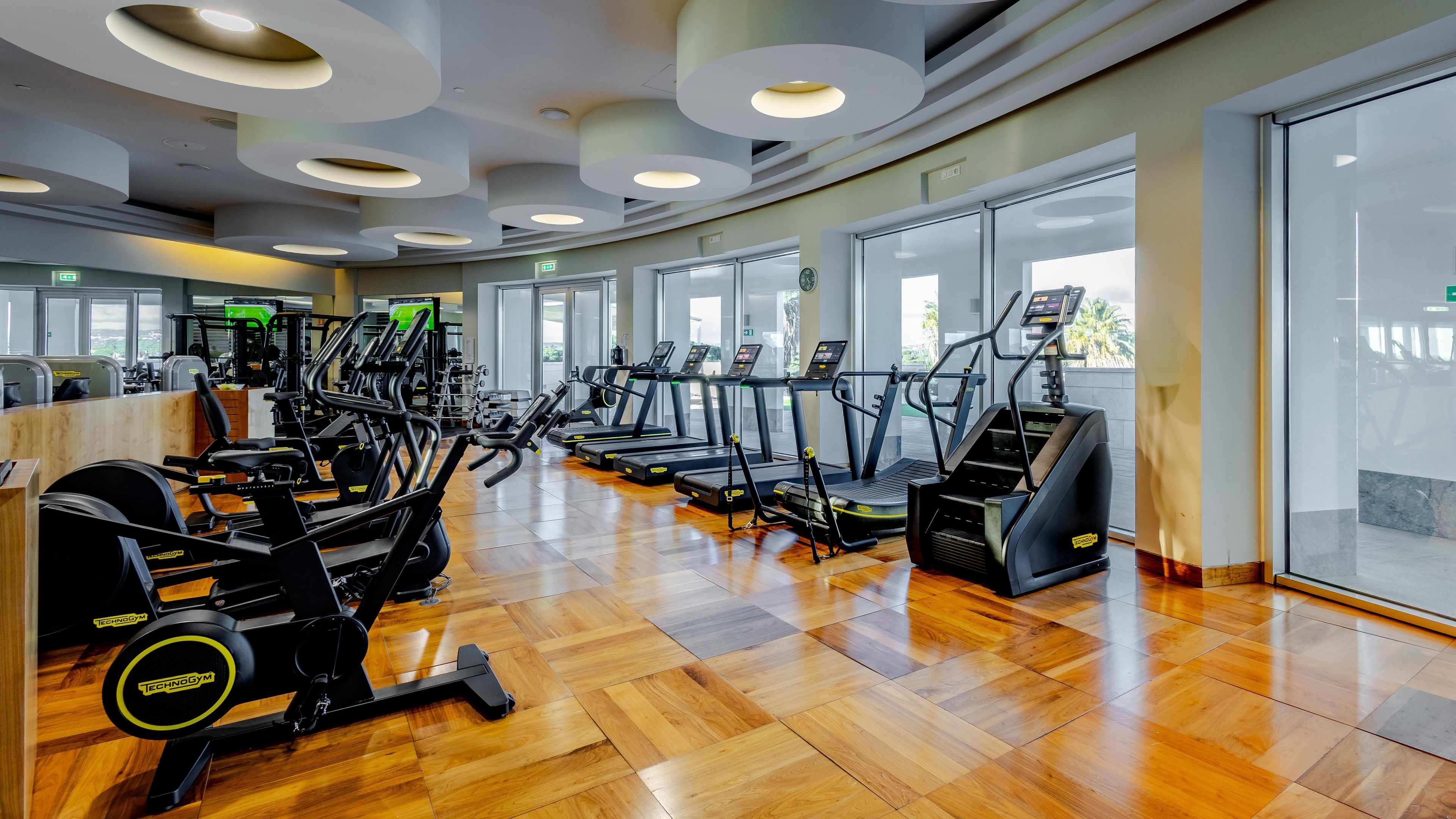 A gym with cardio machines, weight machines, and a wooden floor.