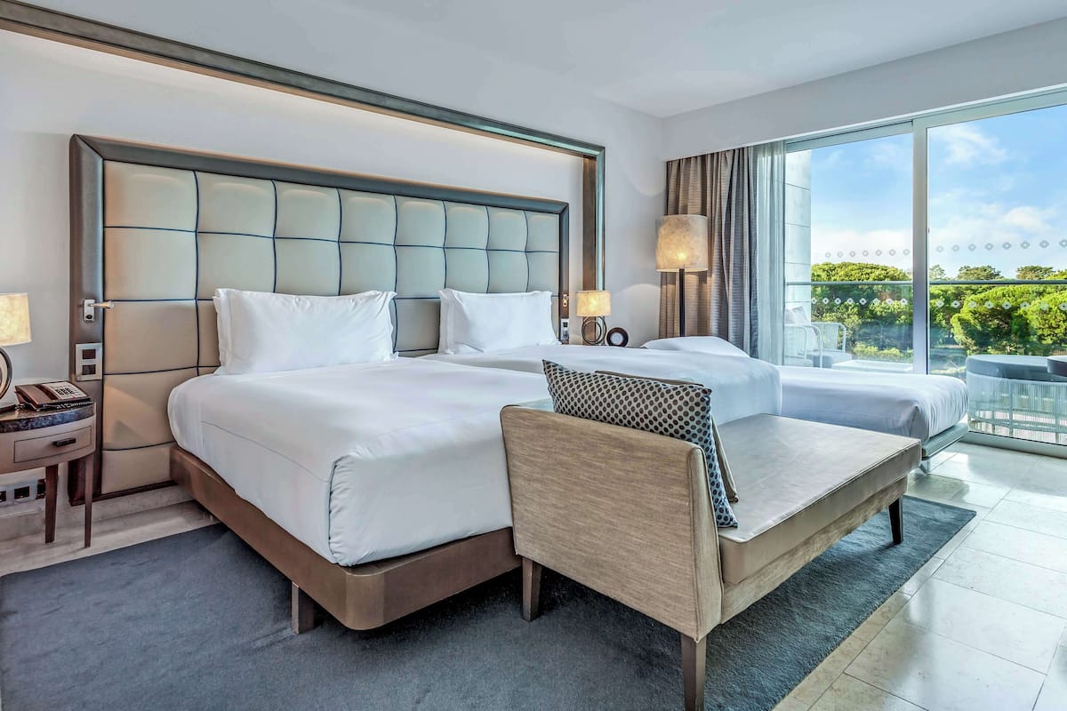 A hotel room with two beds, a sofa, a desk, and a balcony with a view.