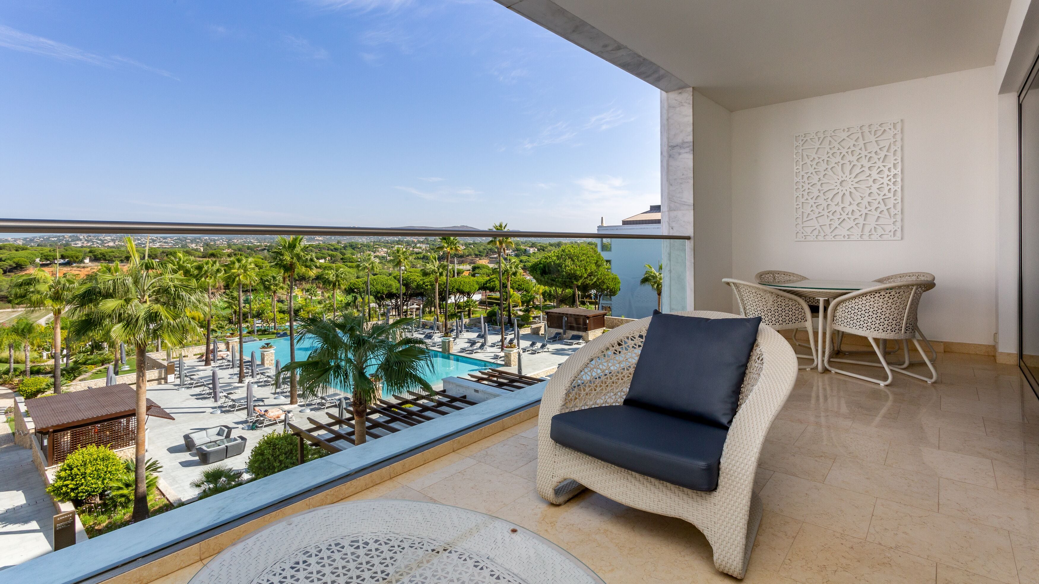 Un balcón con vista a un área de piscina, sillas de descanso y una mesa de comedor.