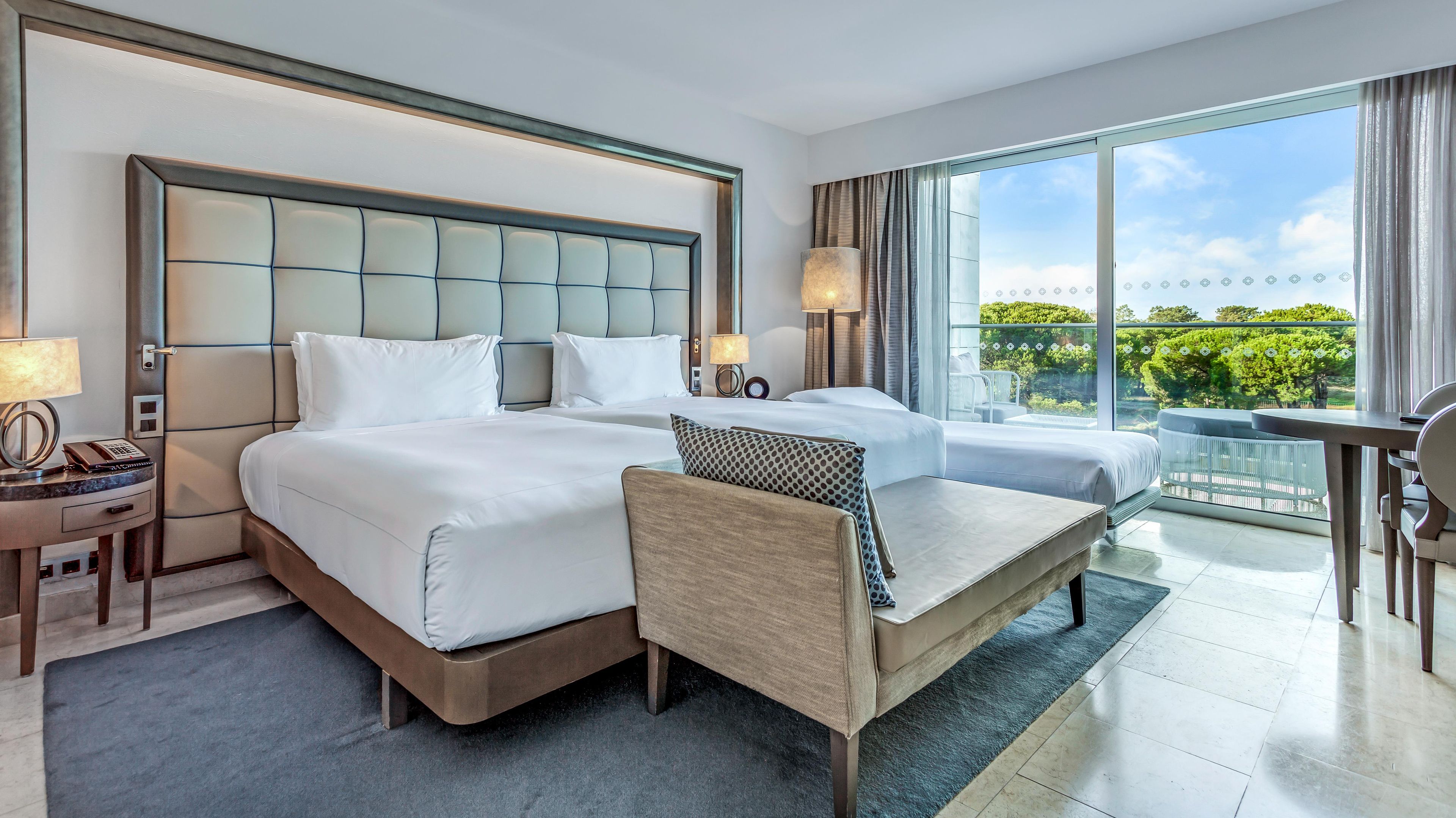 A hotel room with two beds, a sofa, a desk, and a balcony with a view.