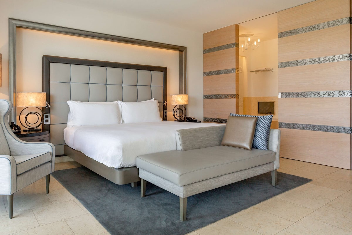 A modern hotel room with a large bed, two bedside tables, a sofa, and a chair.