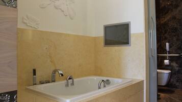 A modern bathroom with a large bathtub, a wall-mounted TV, and a toilet.