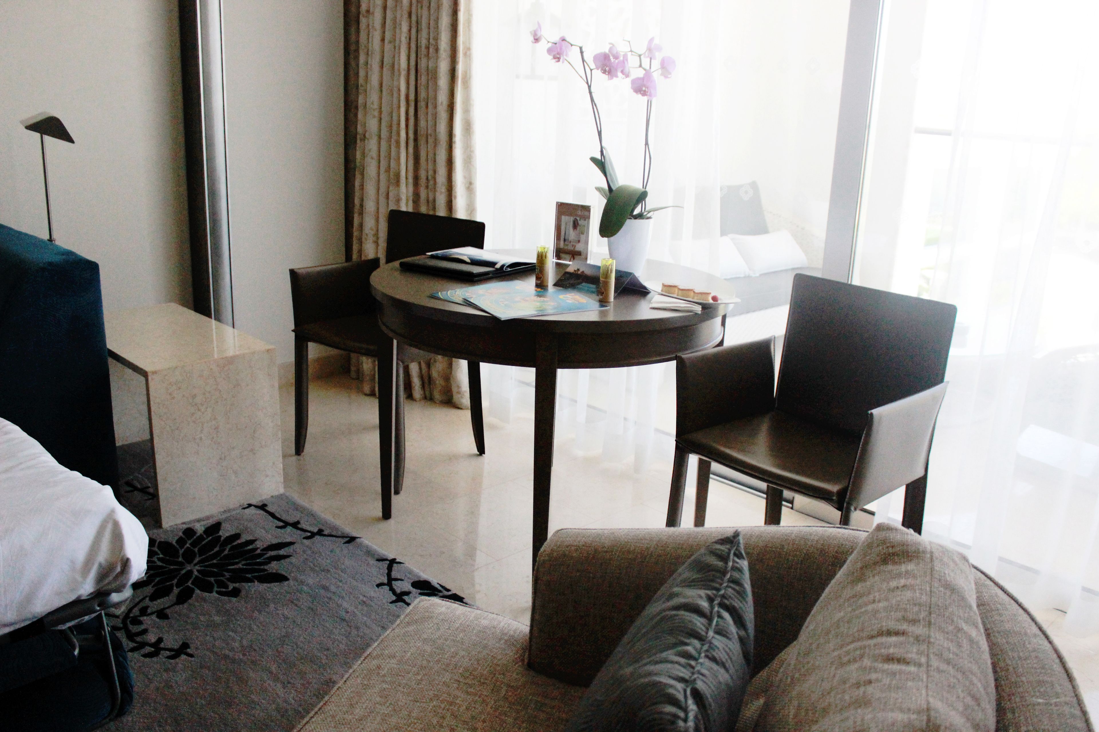 Habitación de hotel con sofá, una mesa de comedor con sillas, una orquídea en maceta y una lámpara.