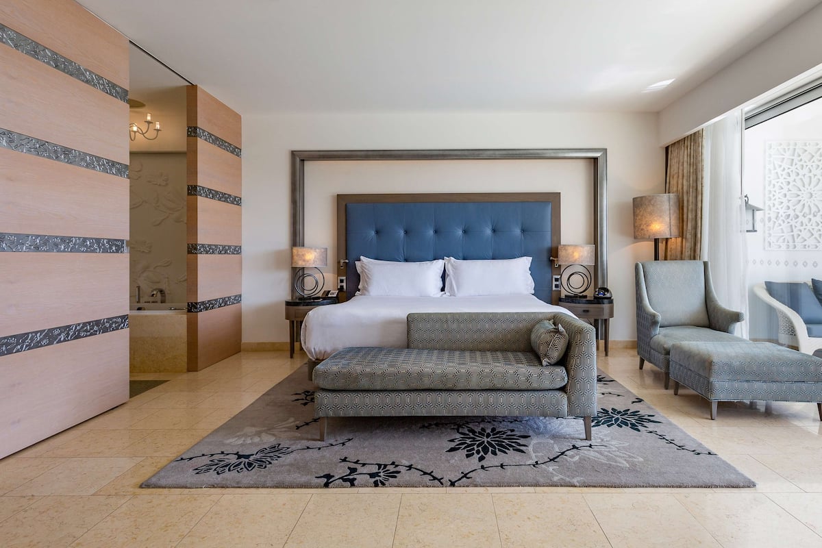 A hotel room with a large bed, a sofa, a chair, and a decorative wall.