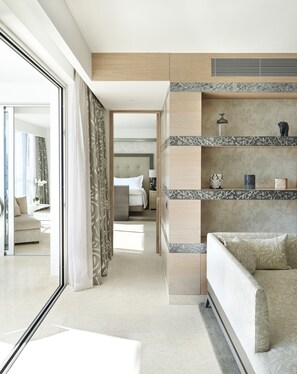 Una habitación de hotel moderna con un ventanal grande, un sofá, una cama y un estante decorativo con objetos.
