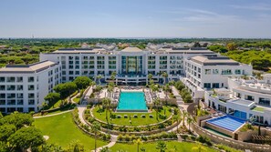 A large hotel with multiple buildings, a central swimming pool, and surrounding greenery.