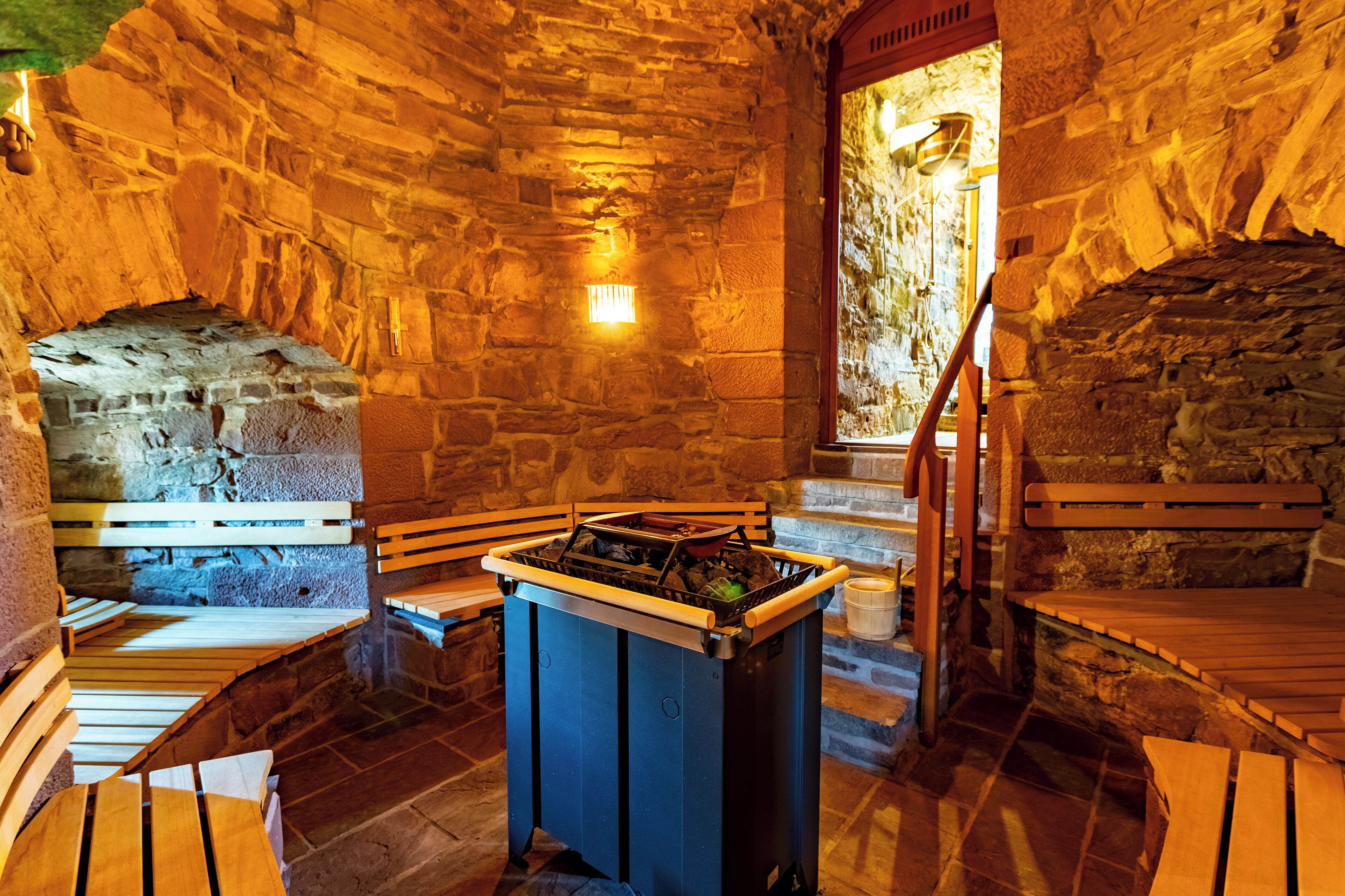 A stone-walled room with a fireplace, wooden benches, and a central table.