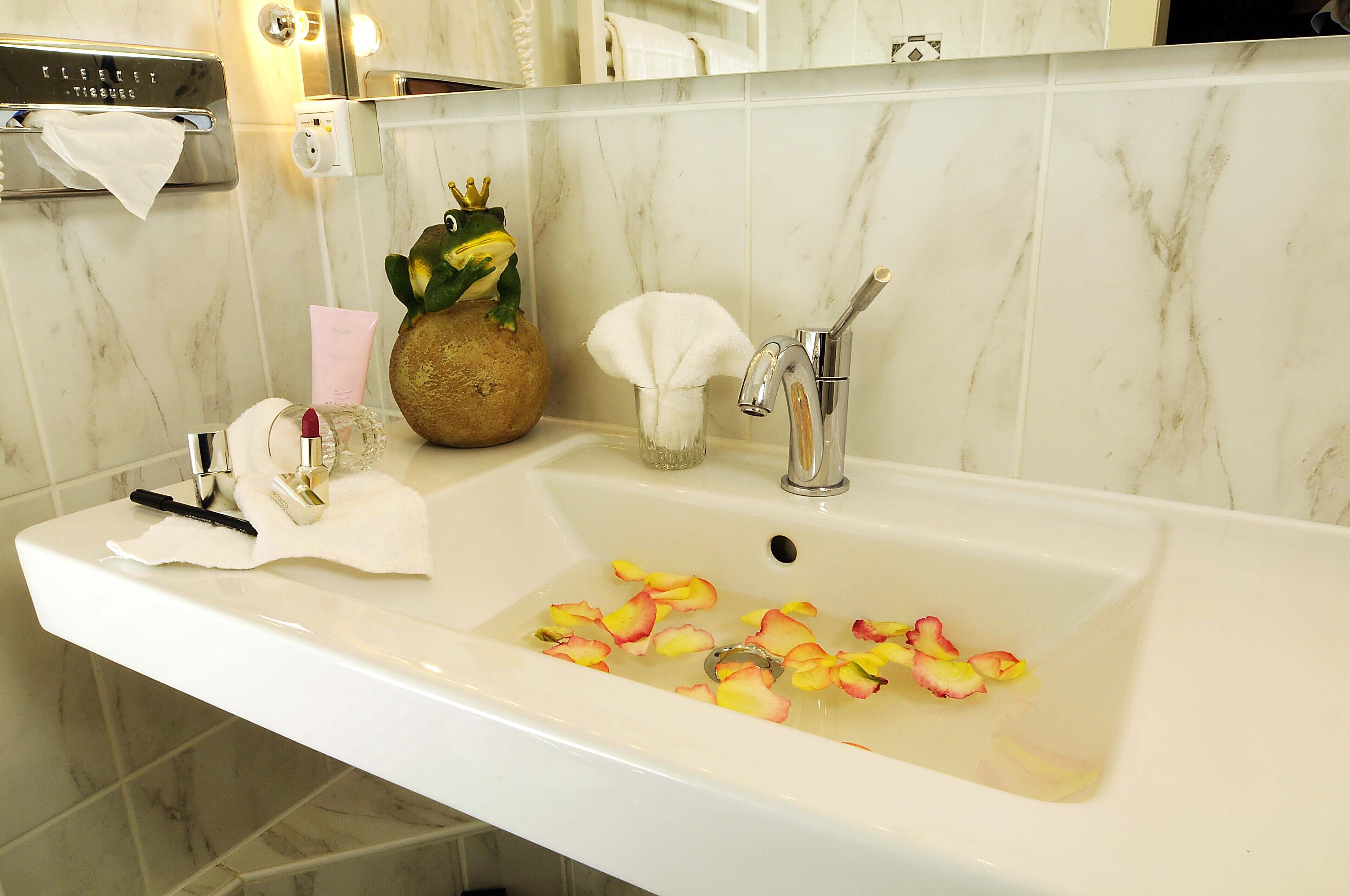 A bathroom sink with a towel rack, a tissue dispenser, and a decorative frog figurine.