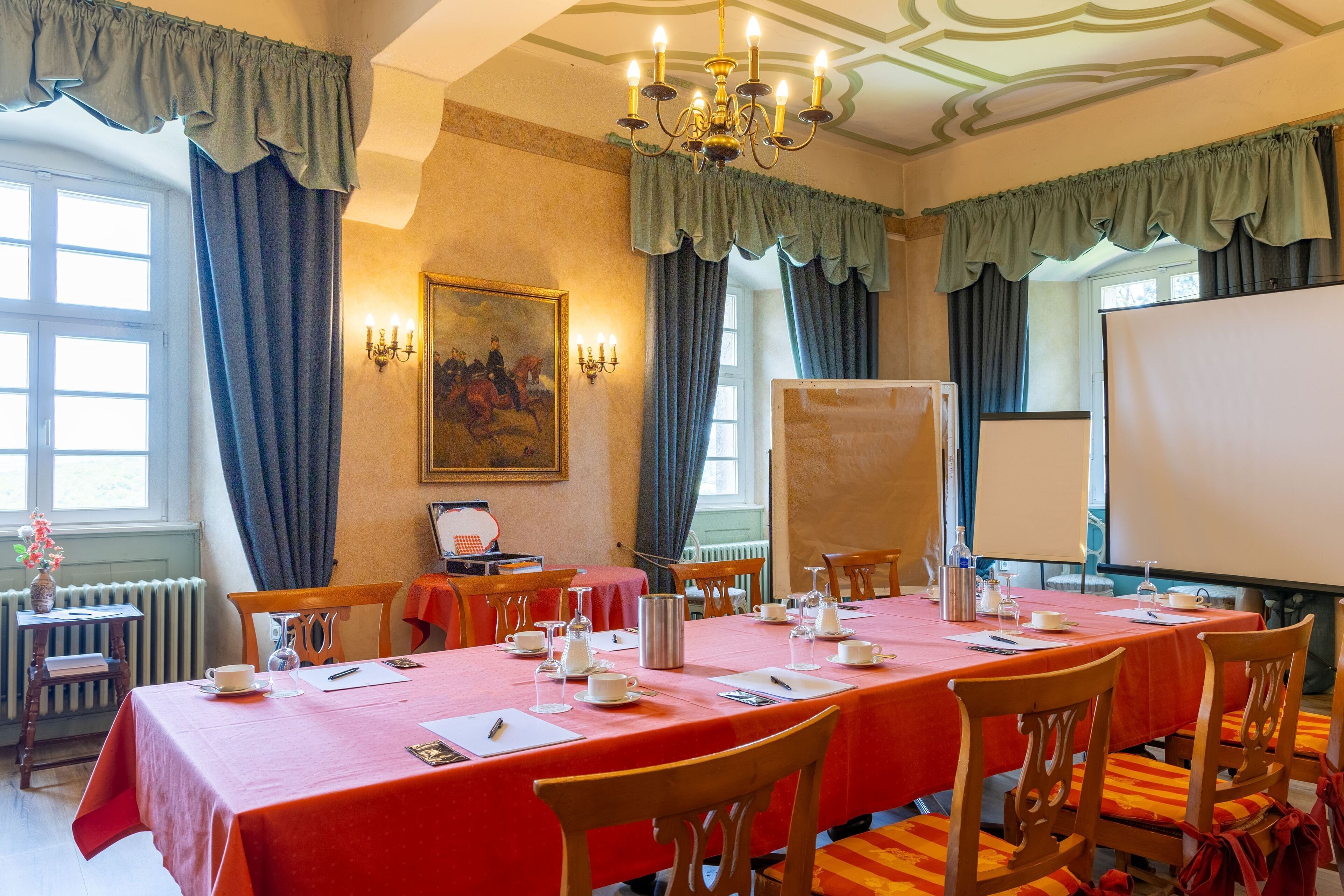 Un salón de conferencias con una larga mesa dispuesta para una reunión, equipado con sillas, un proyector y una pizarra.