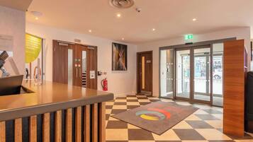 A hotel reception area with a check-in counter, a fire extinguisher, and a glass door leading outside.