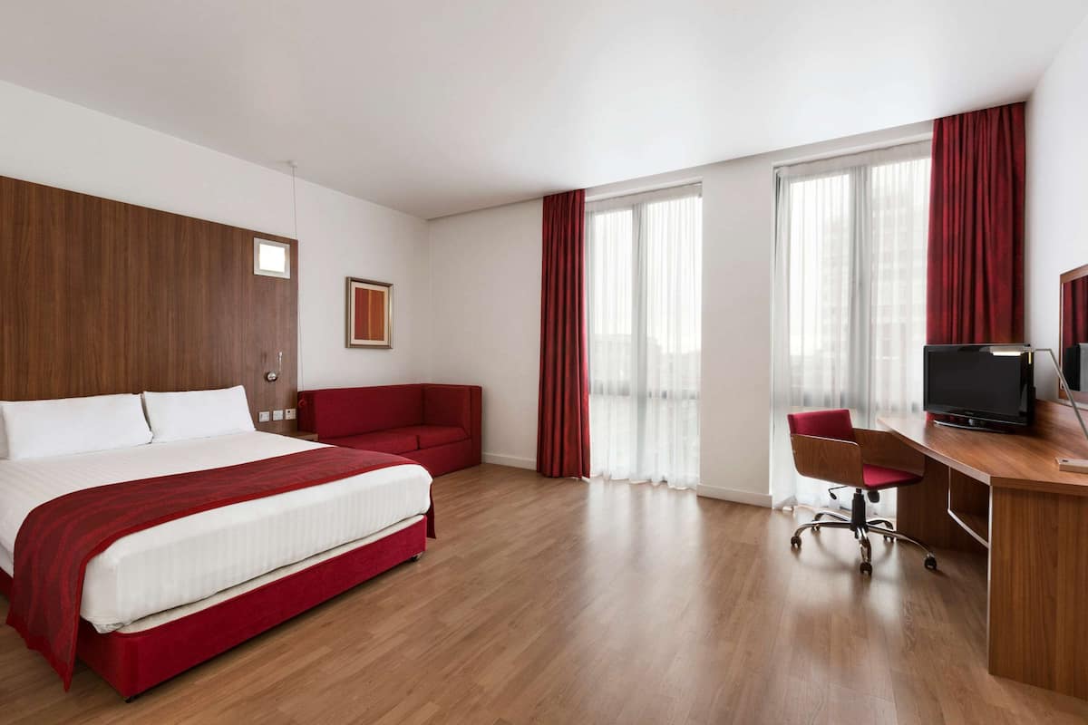A hotel room with a large bed, a desk with a chair, a television, and a red sofa.