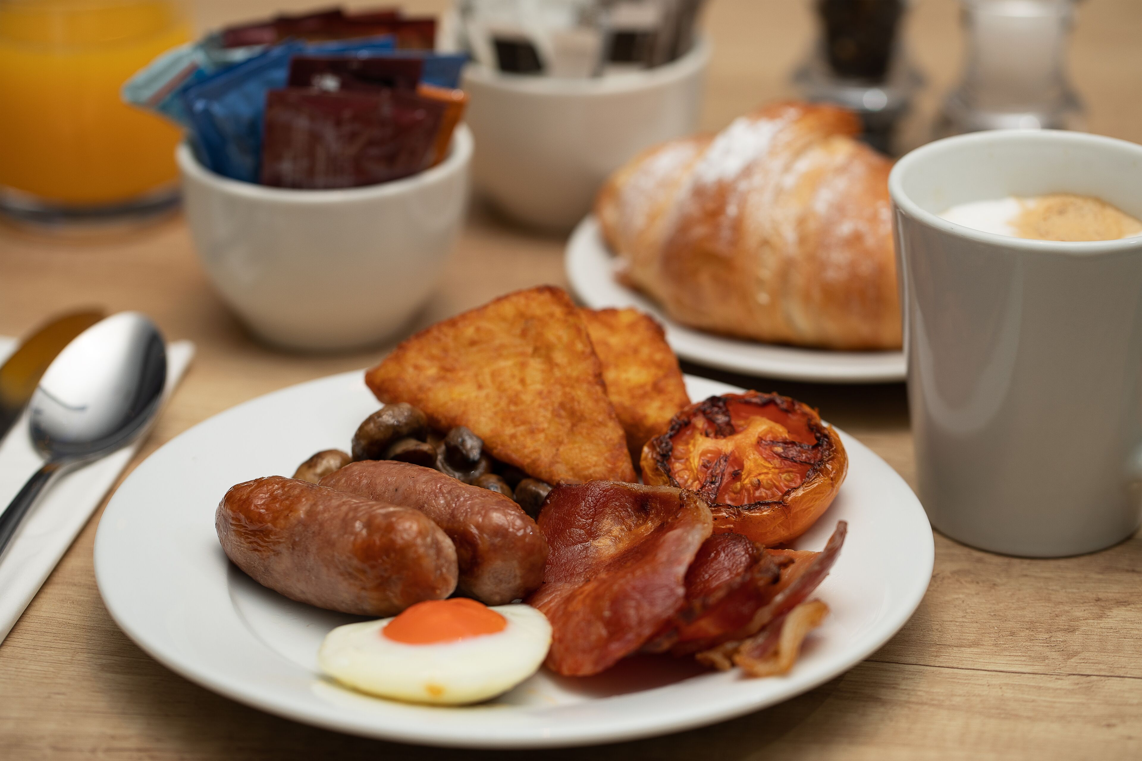 Une assiette de petit-déjeuner comprenant des saucisses, du bacon, des œufs, des champignons et des toasts.